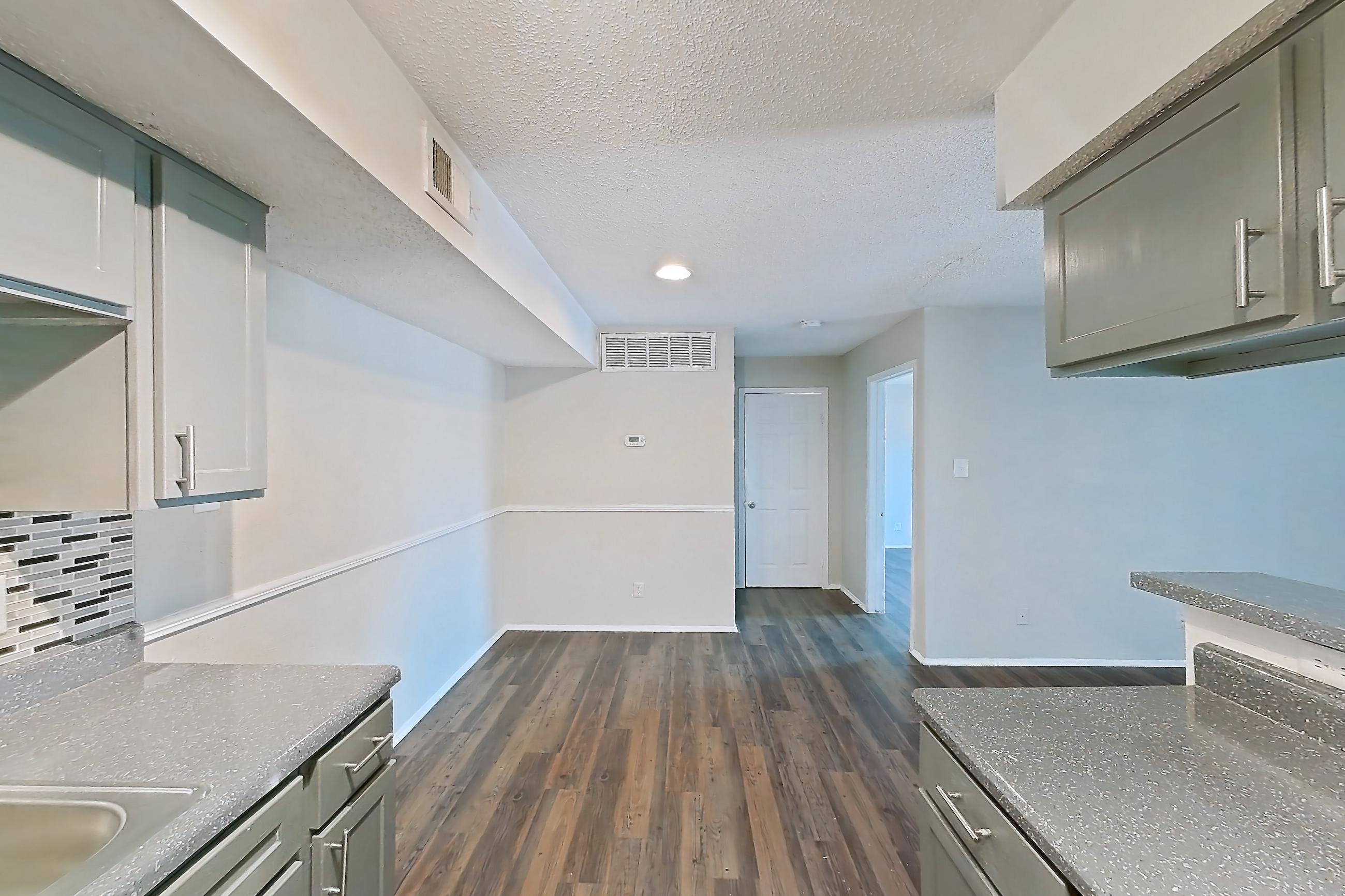 Kitchen with black appliances, dark countertops, dark wood-finish flooring, dishwasher, electric range, light countertops, oven/range, range hood, refrigerator, and stainless steel appliances, Apartment 902 at Marine Creek Apartments