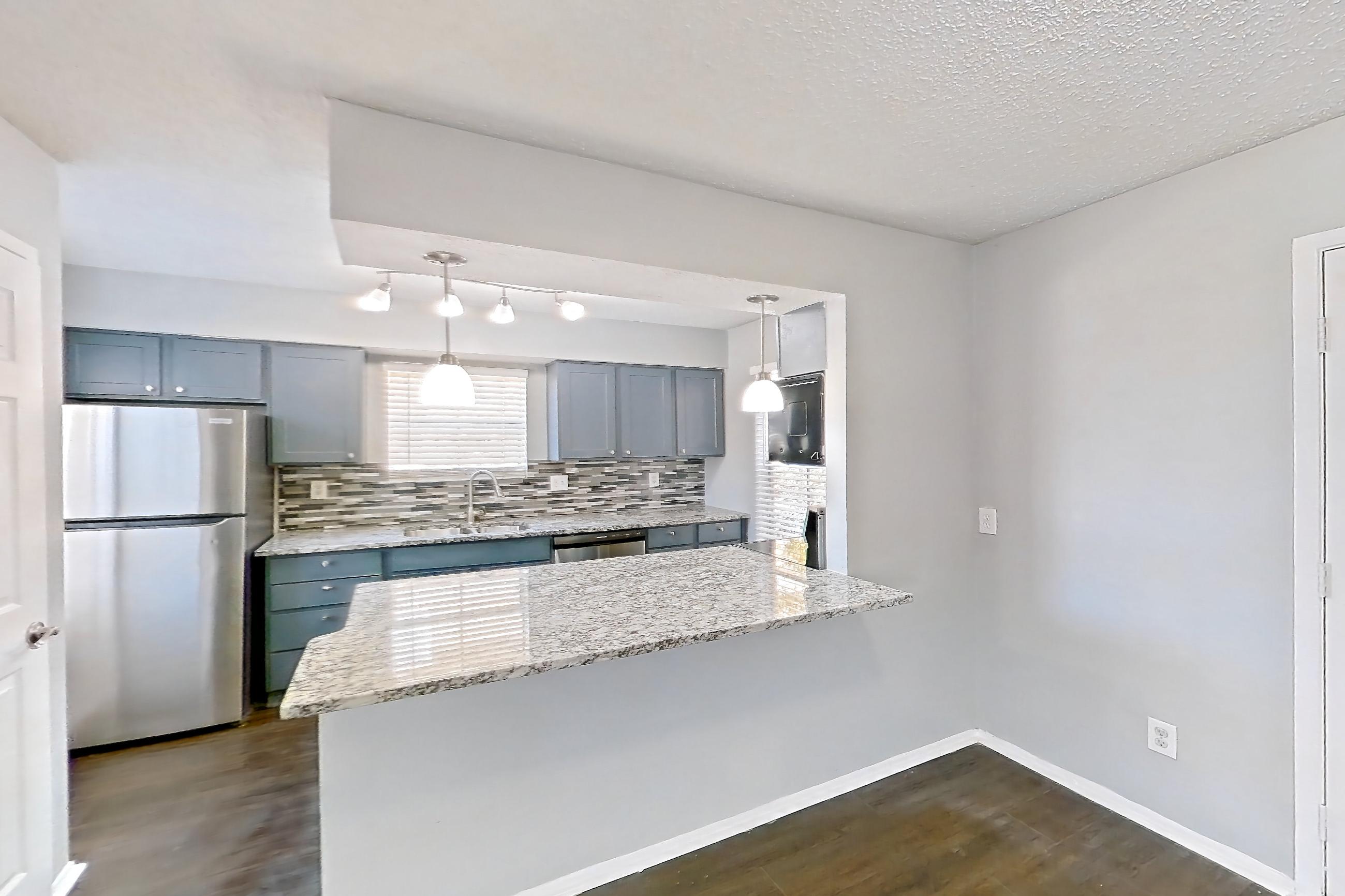 Dining room with dark wood-finish flooring, dishwasher, light countertops, light stone countertops, refrigerator, and stainless steel appliances, Apartment 1207 at Marine Creek Apartments