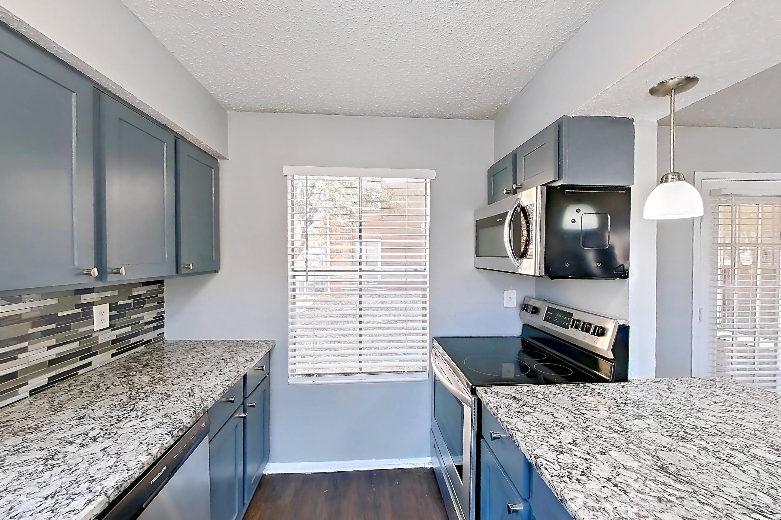 Kitchen with dark wood-finish flooring, dishwasher, electric range, light countertops, light stone countertops, oven/range, and stainless steel appliances, Apartment 1207 at Marine Creek Apartments