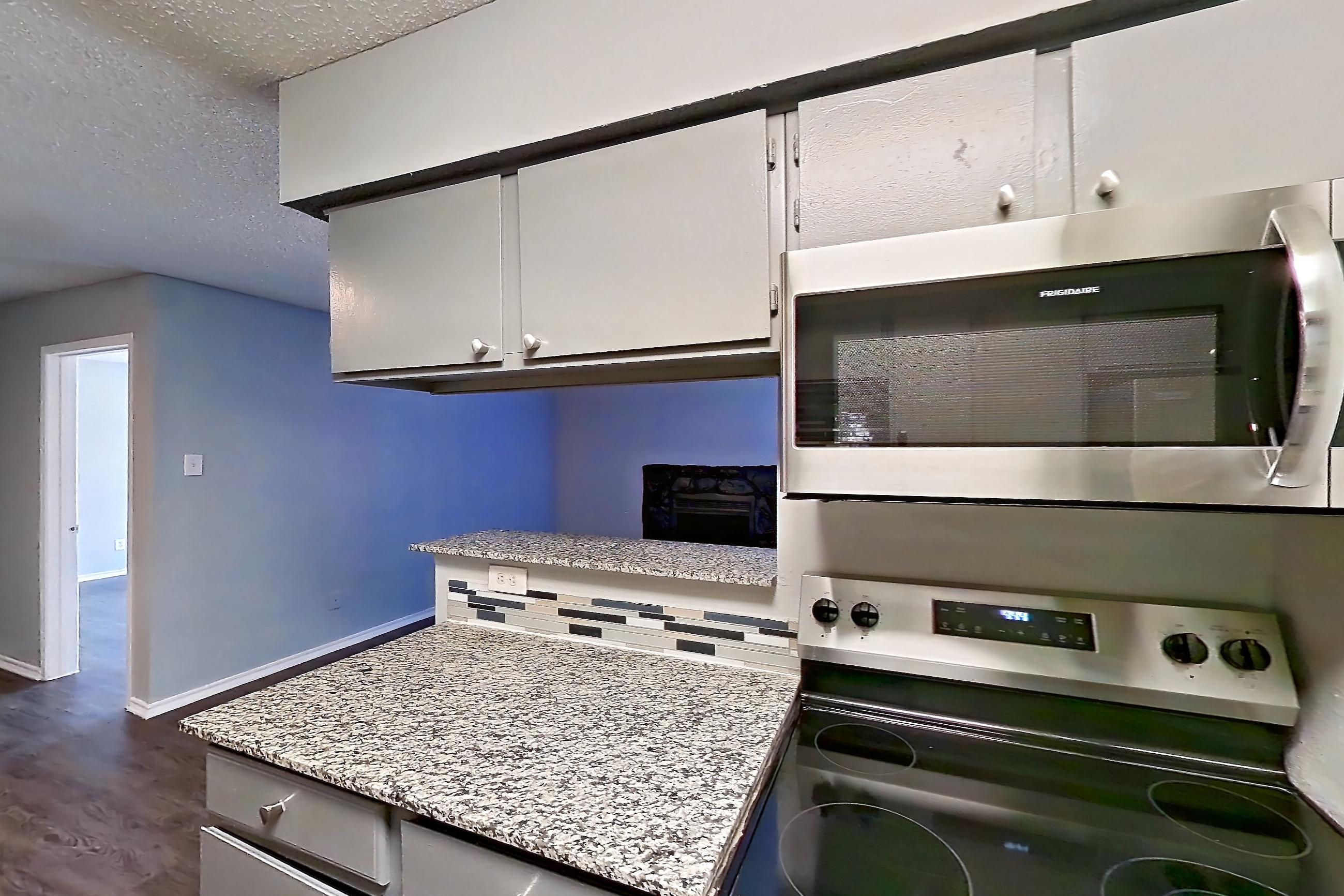Kitchen with dark wood-finish flooring, dishwasher, electric range, light countertops, light stone countertops, microwave, oven/range, and stainless steel appliances, Apartment 1505 at Marine Creek Apartments