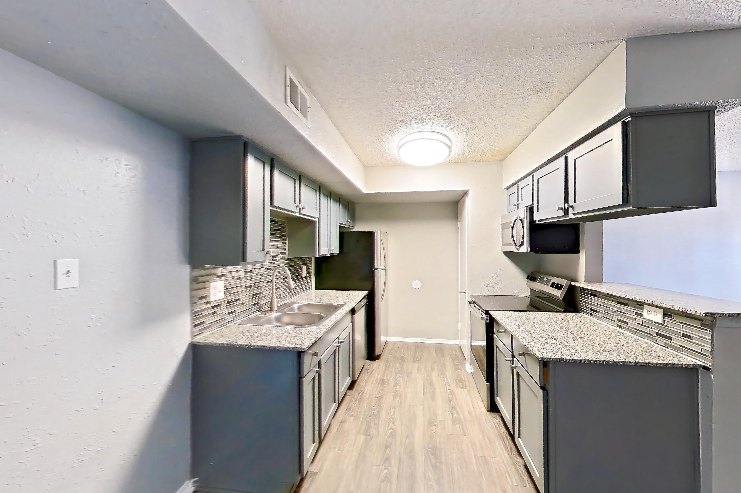 Dining room with dark wood-finish flooring, dishwasher, electric range, fireplace, light countertops, light stone countertops, light wood-finish flooring, oven/range, stainless steel appliances, and stone fireplace, Apartment 1801 at Marine Creek Apartments