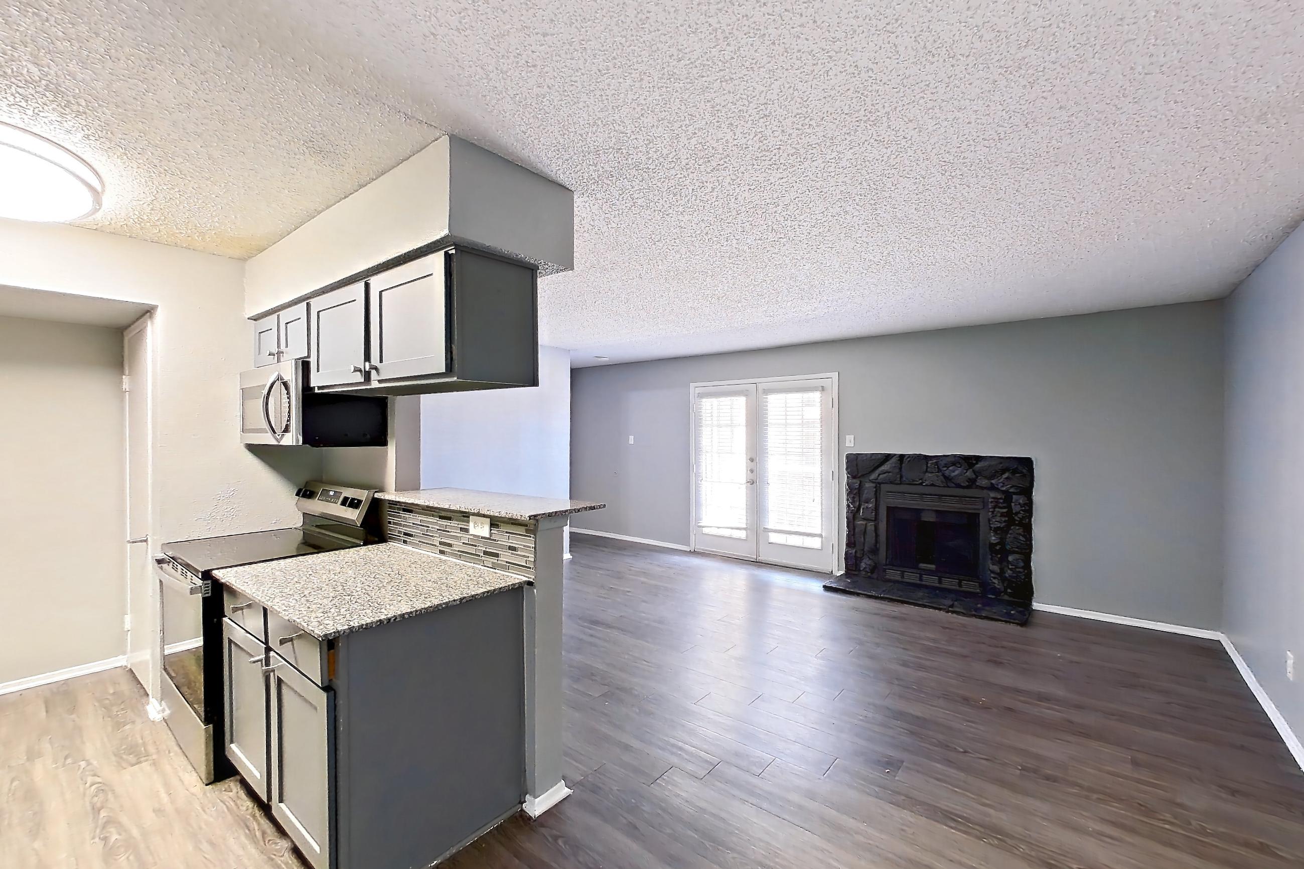 Dining room with dark wood-finish flooring, dishwasher, electric range, fireplace, light countertops, light stone countertops, light wood-finish flooring, oven/range, stainless steel appliances, and stone fireplace, Apartment 1801 at Marine Creek Apartments