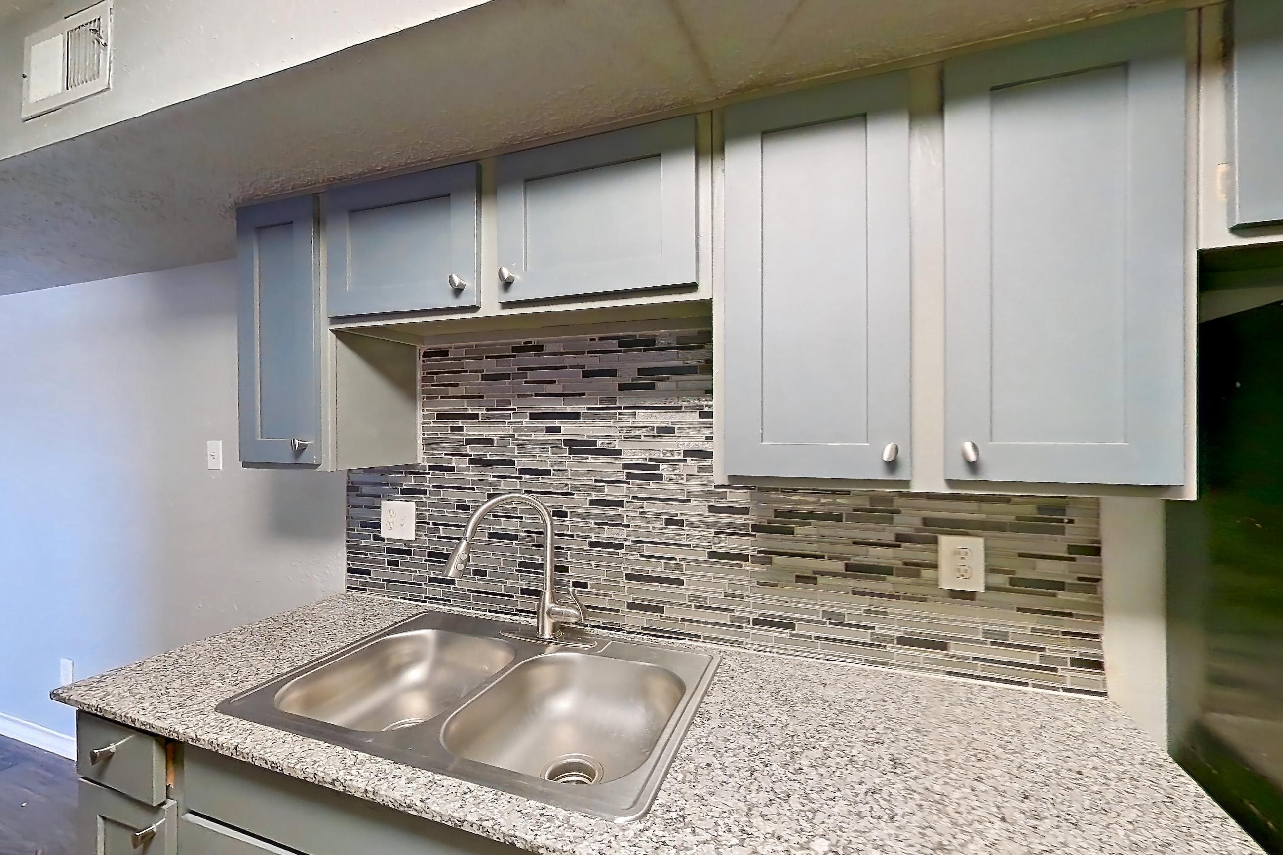 Kitchen with dark wood-finish flooring, dishwasher, electric range, light countertops, light stone countertops, light wood-finish flooring, microwave, oven/range, refrigerator, and stainless steel appliances, Apartment 1801 at Marine Creek Apartments