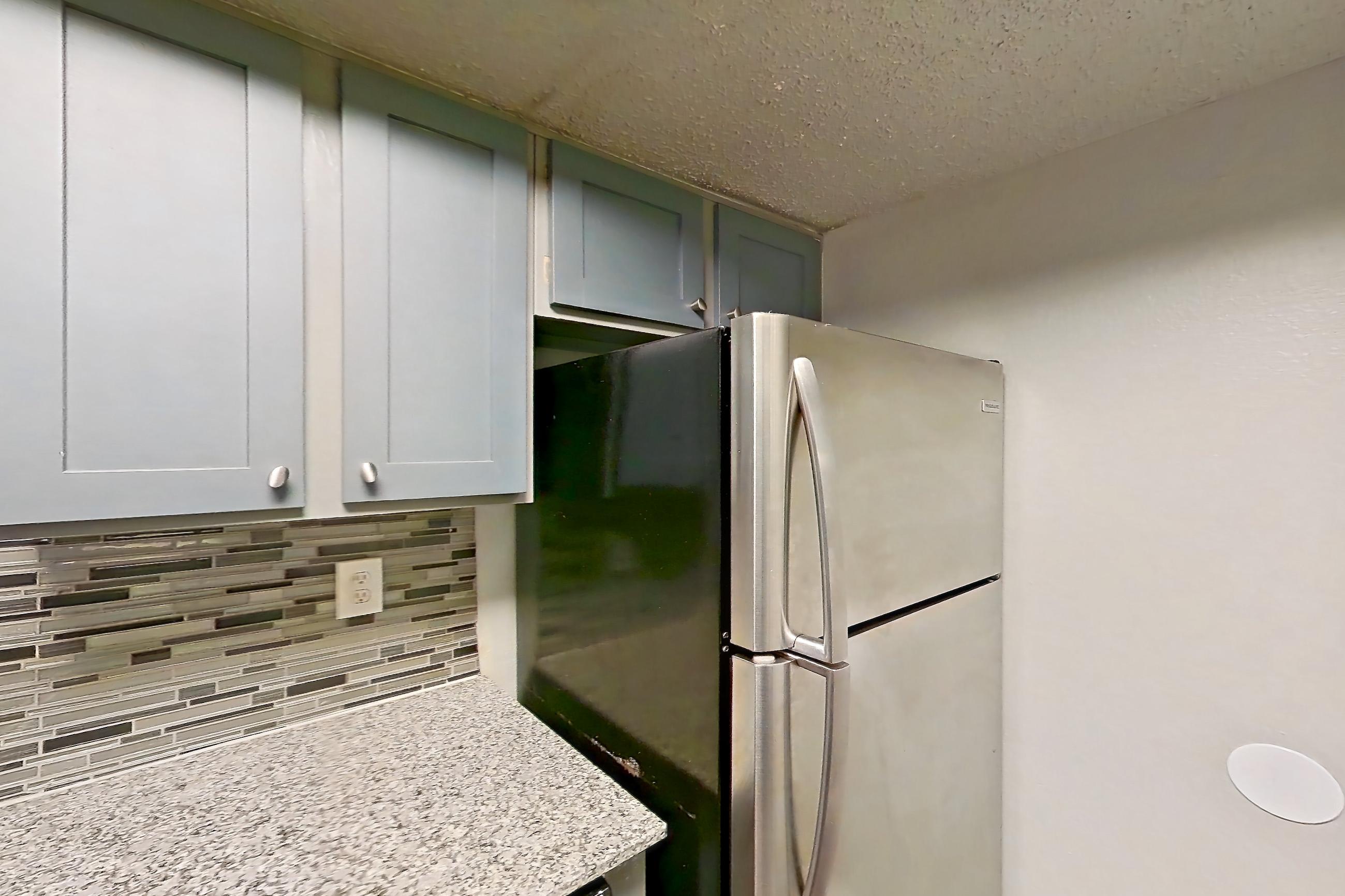 Kitchen with dark wood-finish flooring, dishwasher, electric range, light countertops, light stone countertops, light wood-finish flooring, microwave, oven/range, refrigerator, and stainless steel appliances, Apartment 1801 at Marine Creek Apartments