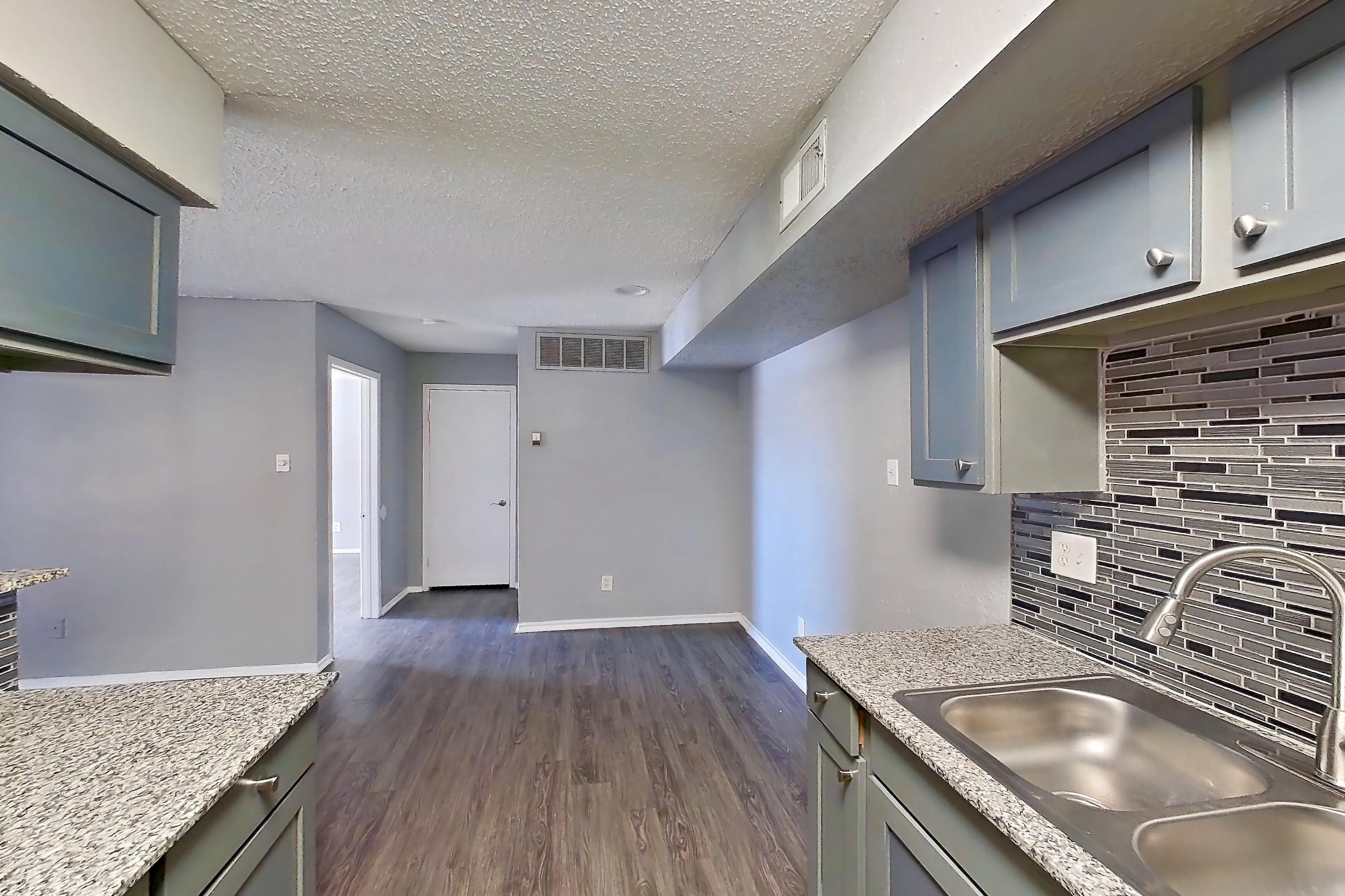 Kitchen with dark wood-finish flooring, dishwasher, electric range, light countertops, light stone countertops, light wood-finish flooring, microwave, oven/range, refrigerator, and stainless steel appliances, Apartment 1801 at Marine Creek Apartments