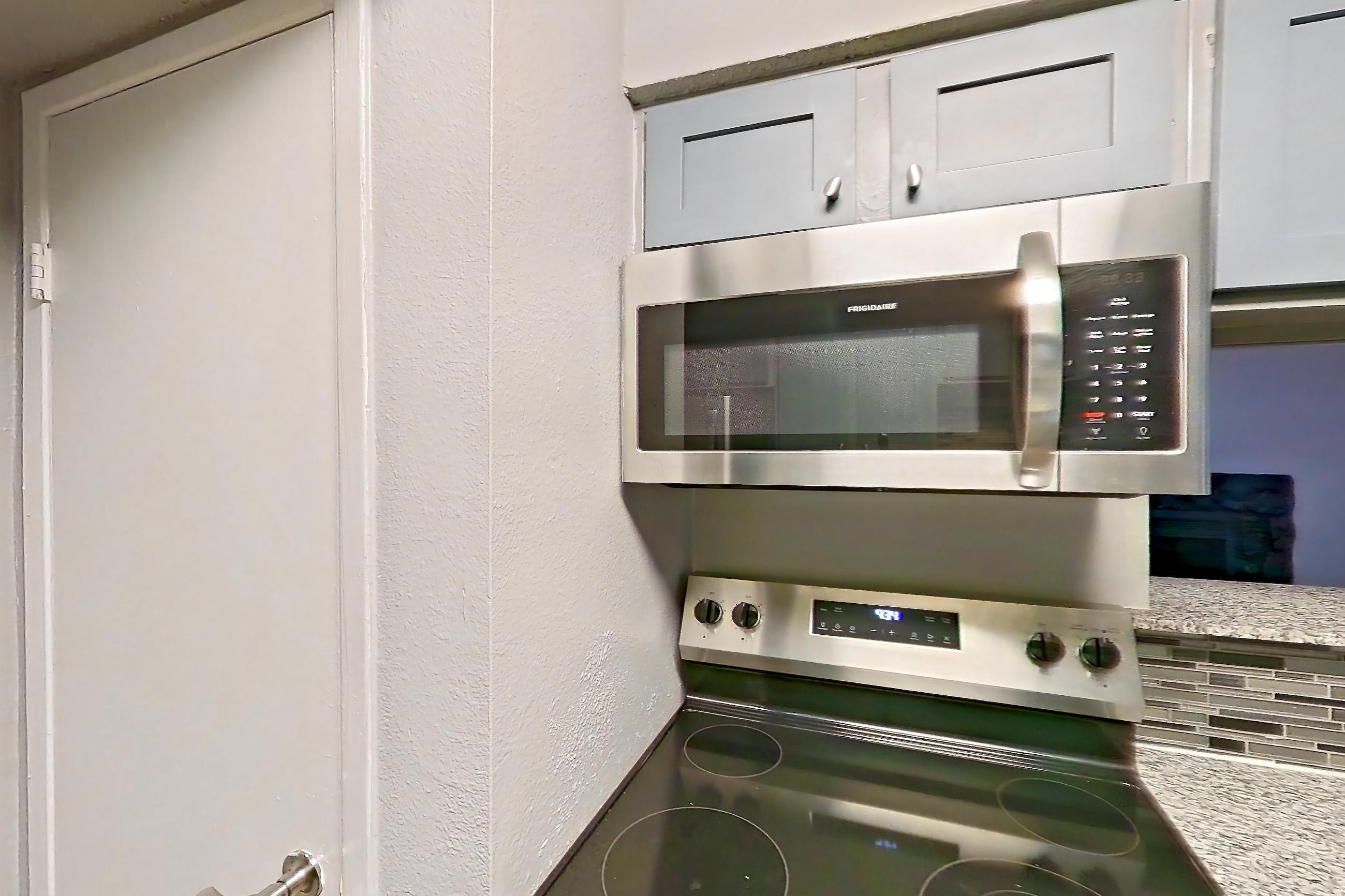 Kitchen with dark wood-finish flooring, dishwasher, electric range, light countertops, light stone countertops, light wood-finish flooring, microwave, oven/range, refrigerator, and stainless steel appliances, Apartment 1801 at Marine Creek Apartments