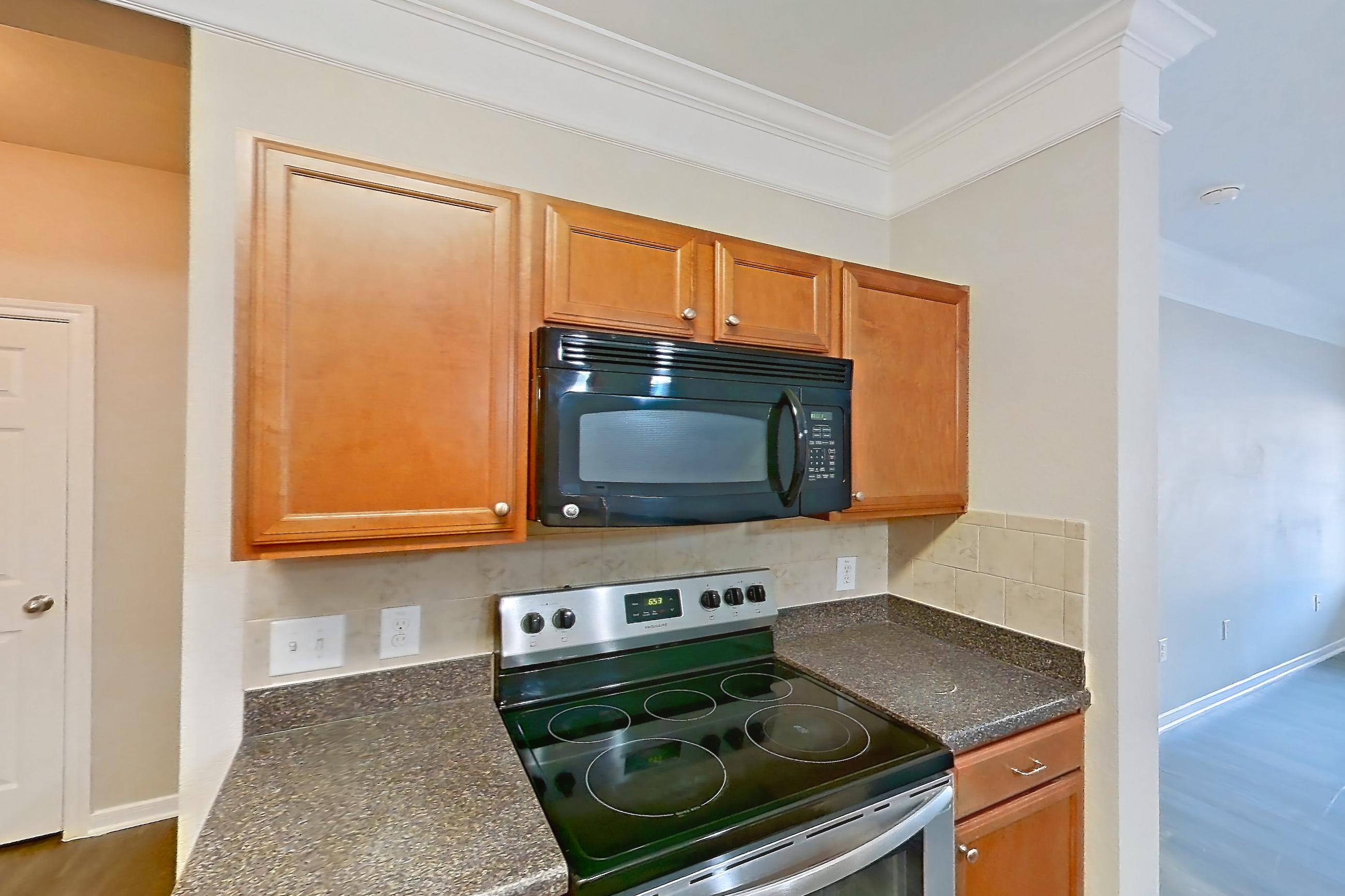 Kitchen with black appliances, dark countertops, dark stone countertops, dark wood-finish flooring, dishwasher, electric range, light wood-finish flooring, microwave, oven/range, refrigerator, and stainless steel appliances, Apartment 5103 at Terraces at Fall Creek