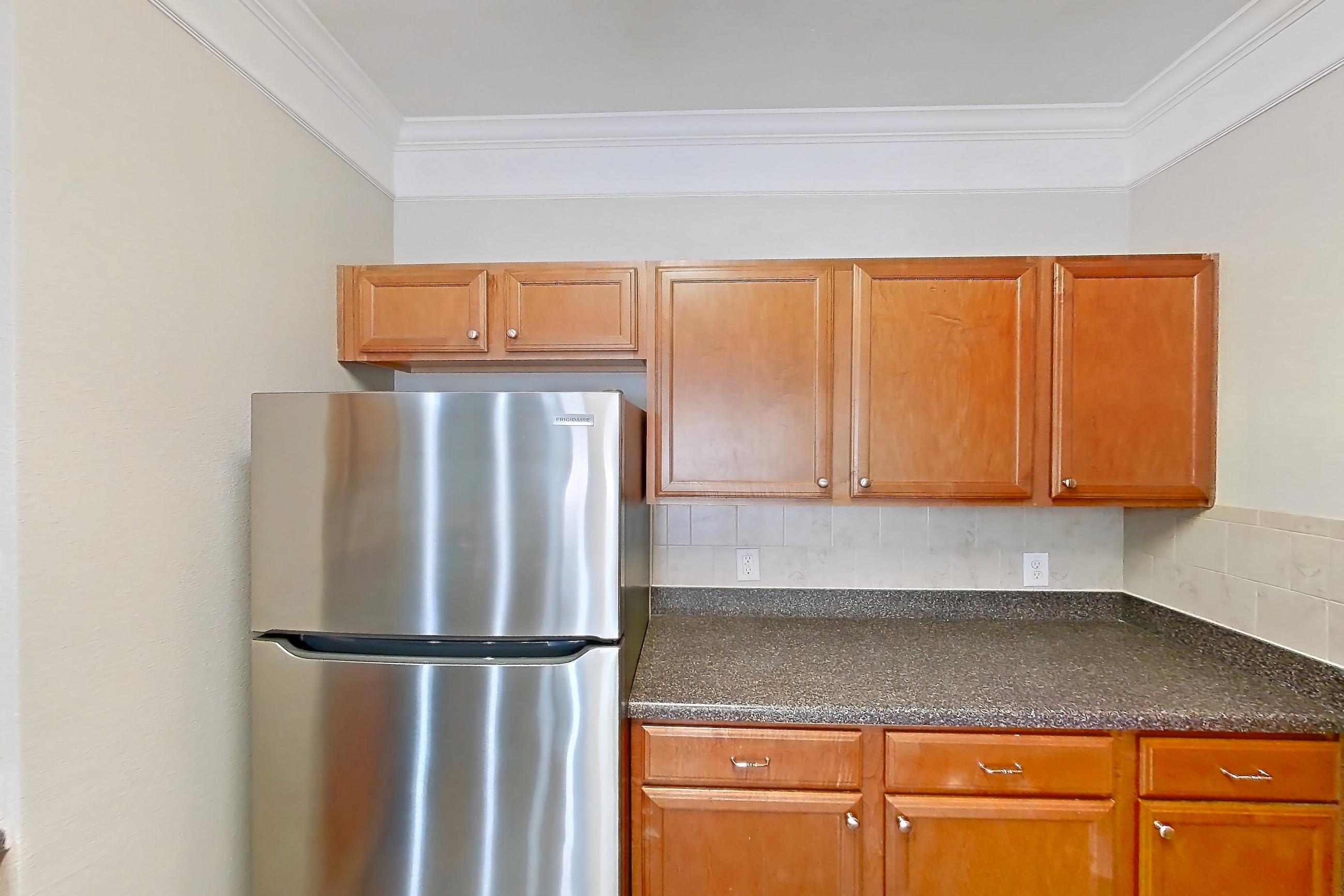 Kitchen with black appliances, dark countertops, dark stone countertops, dark wood-finish flooring, dishwasher, electric range, light wood-finish flooring, microwave, oven/range, refrigerator, and stainless steel appliances, Apartment 5103 at Terraces at Fall Creek