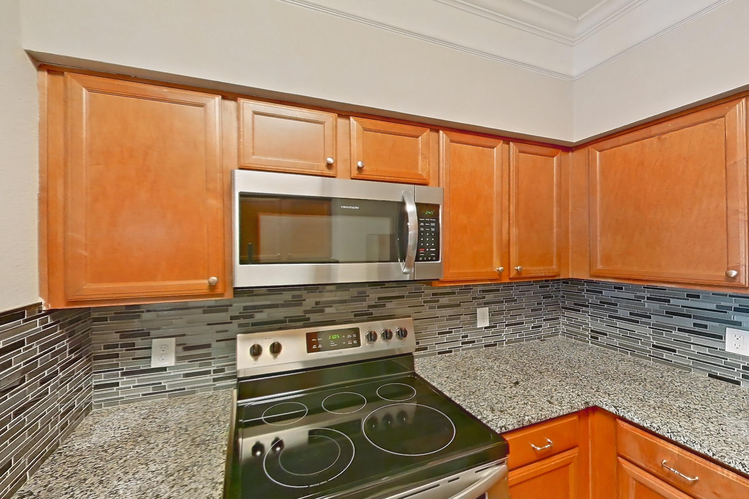 Kitchen with dark wood-finish flooring, dishwasher, electric range, light countertops, light stone countertops, microwave, oven/range, refrigerator, and stainless steel appliances, Apartment 5104 at Terraces at Fall Creek