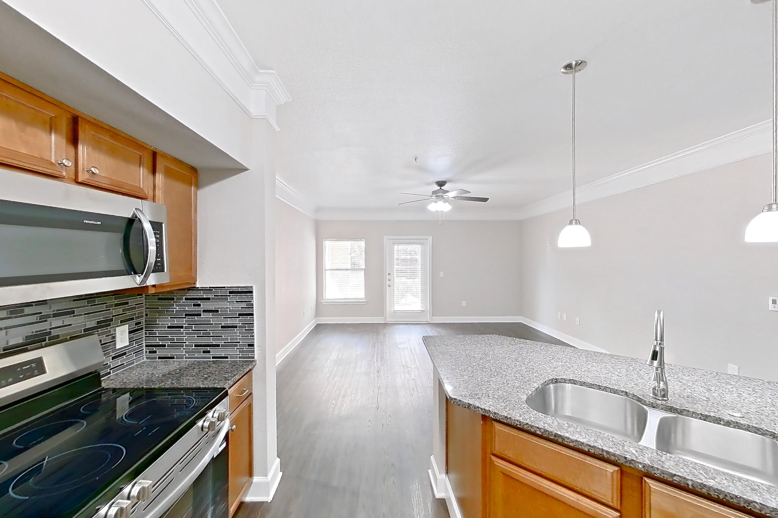 Kitchen with dark stone countertops, dark wood-finish flooring, dishwasher, electric range, light stone countertops, microwave, oven/range, refrigerator, stainless steel appliances, and white appliances, Apartment 8102 at Terraces at Fall Creek