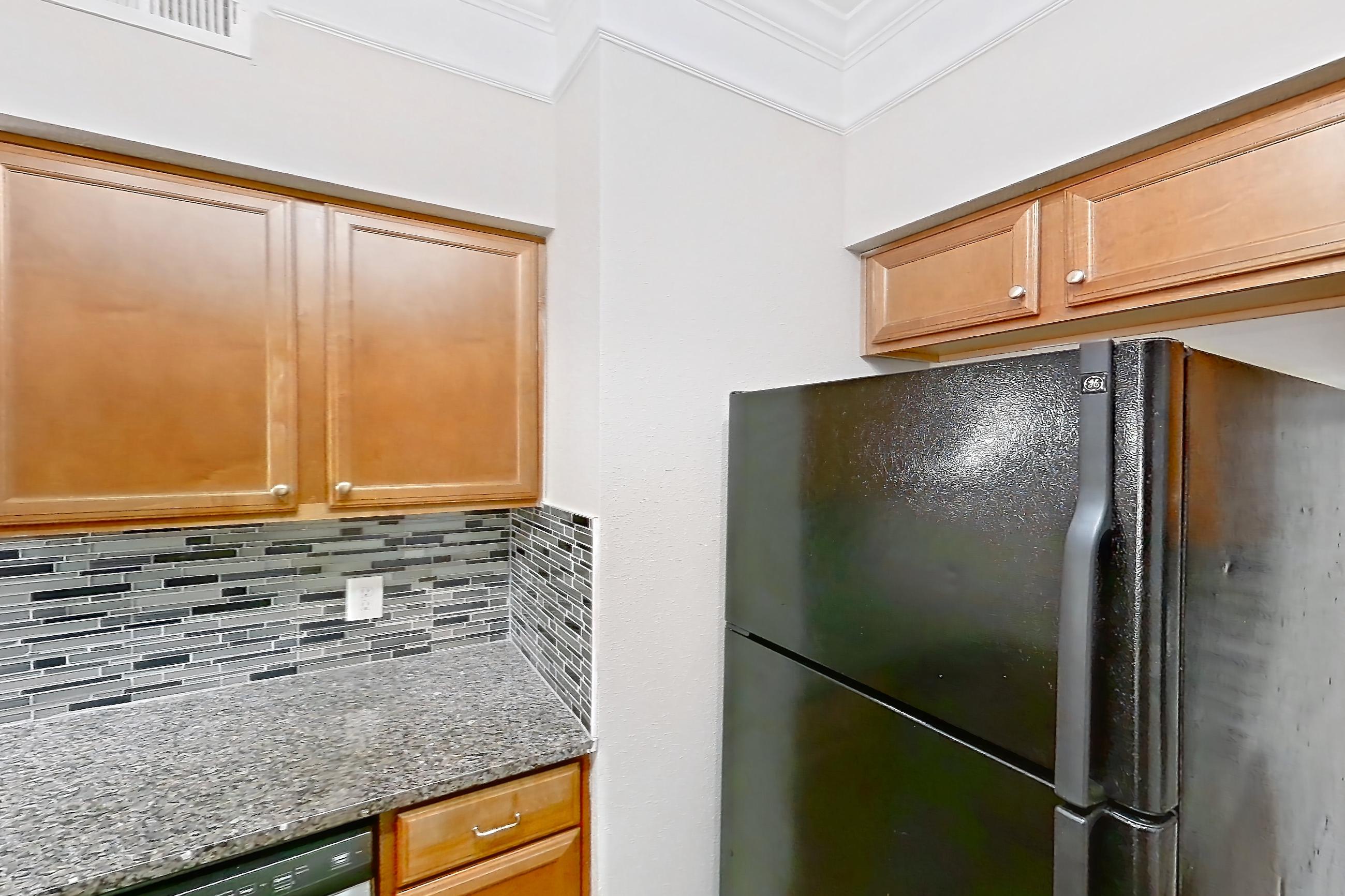 Kitchen with dark stone countertops, dark wood-finish flooring, dishwasher, electric range, light stone countertops, microwave, oven/range, refrigerator, stainless steel appliances, and white appliances, Apartment 8102 at Terraces at Fall Creek