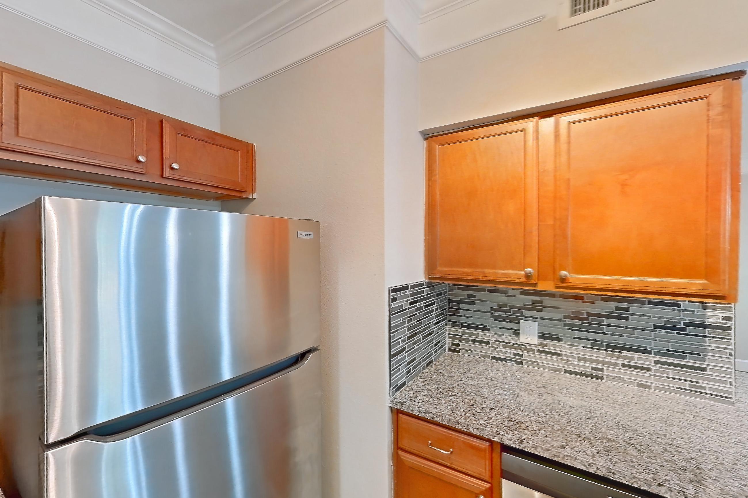 Kitchen with dark stone countertops, dark wood-finish flooring, dishwasher, electric range, light countertops, light stone countertops, light wood-finish flooring, microwave, oven/range, refrigerator, and stainless steel appliances, Apartment 10108 at Terraces at Fall Creek