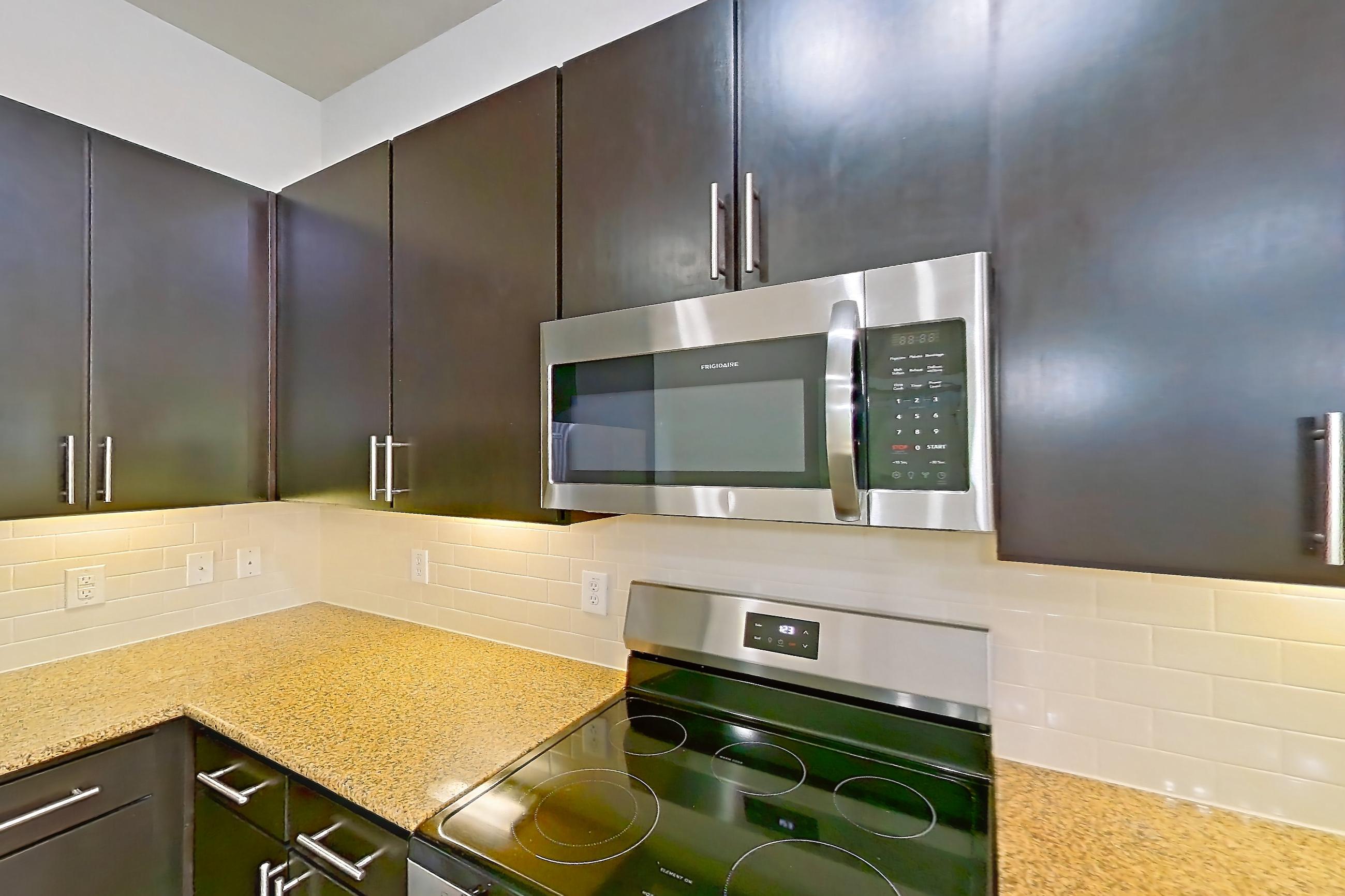 Kitchen with electric range, light stone countertops, light wood-finish flooring, microwave, oven/range, and stainless steel appliances, Apartment 110 at Voyager at the Space Center