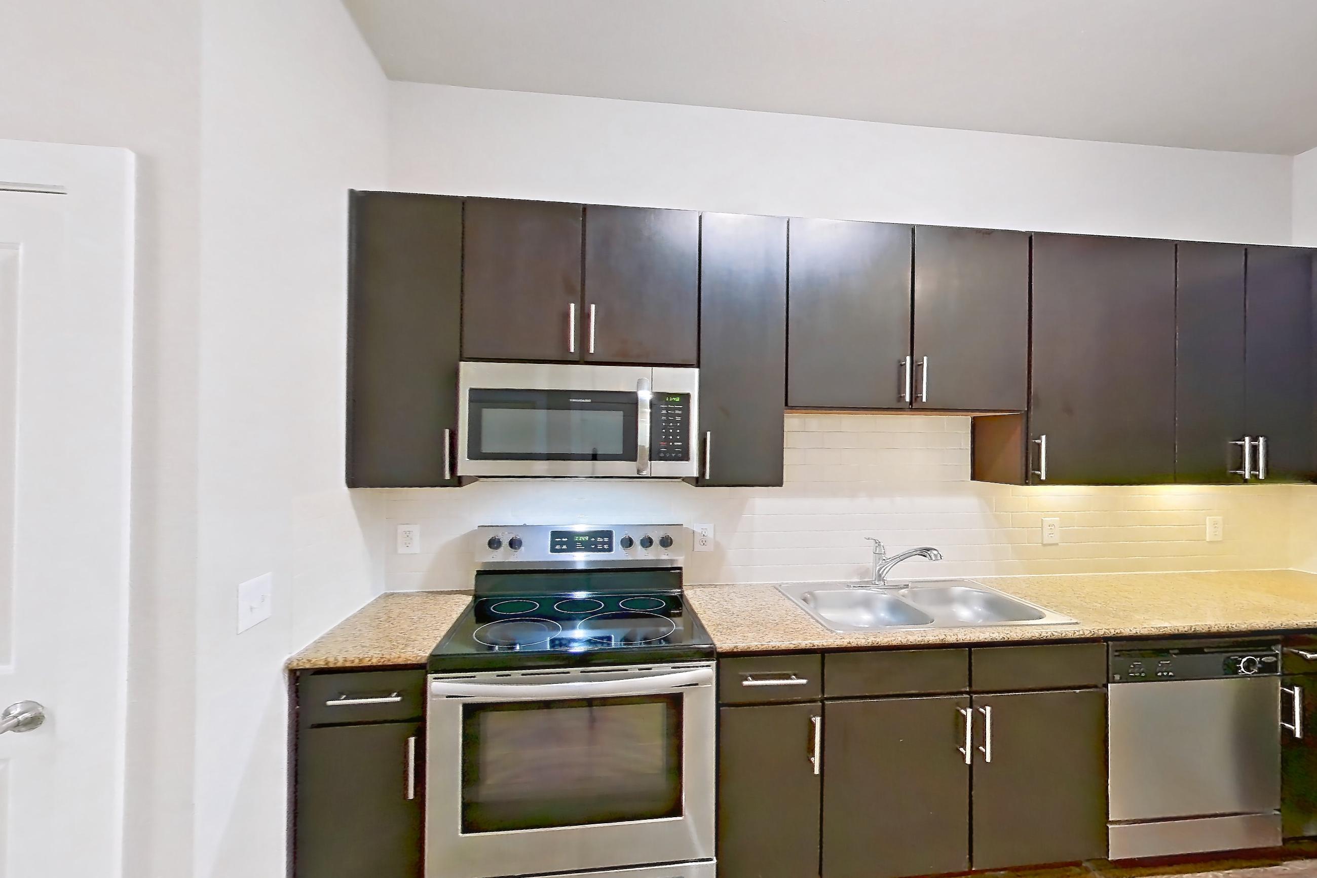 Kitchen space with electric range, light stone countertops, light wood-finish flooring, microwave, oven/range, and stainless steel appliances, Apartment 125 at Voyager at the Space Center