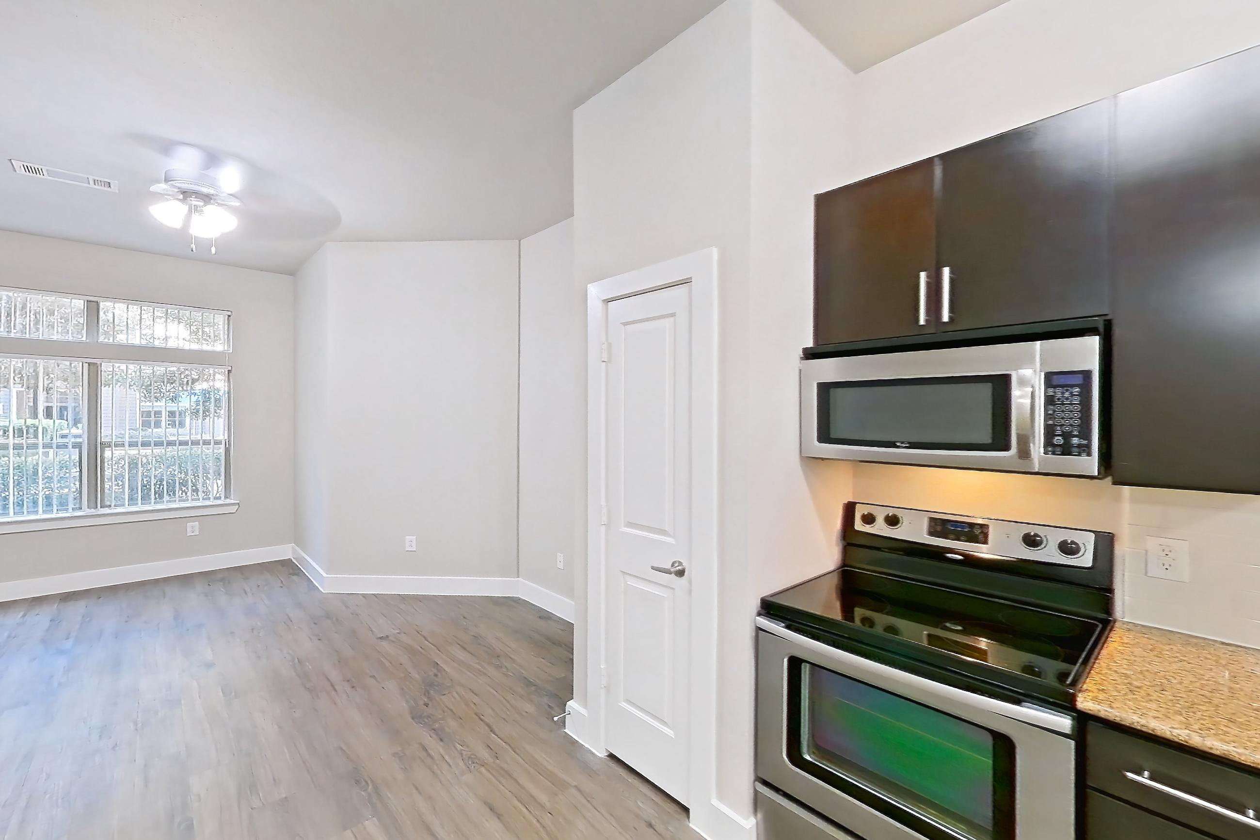 Kitchen space with electric range, light countertops, light wood-finish flooring, microwave, oven/range, and stainless steel appliances, Apartment 140 at Voyager at the Space Center