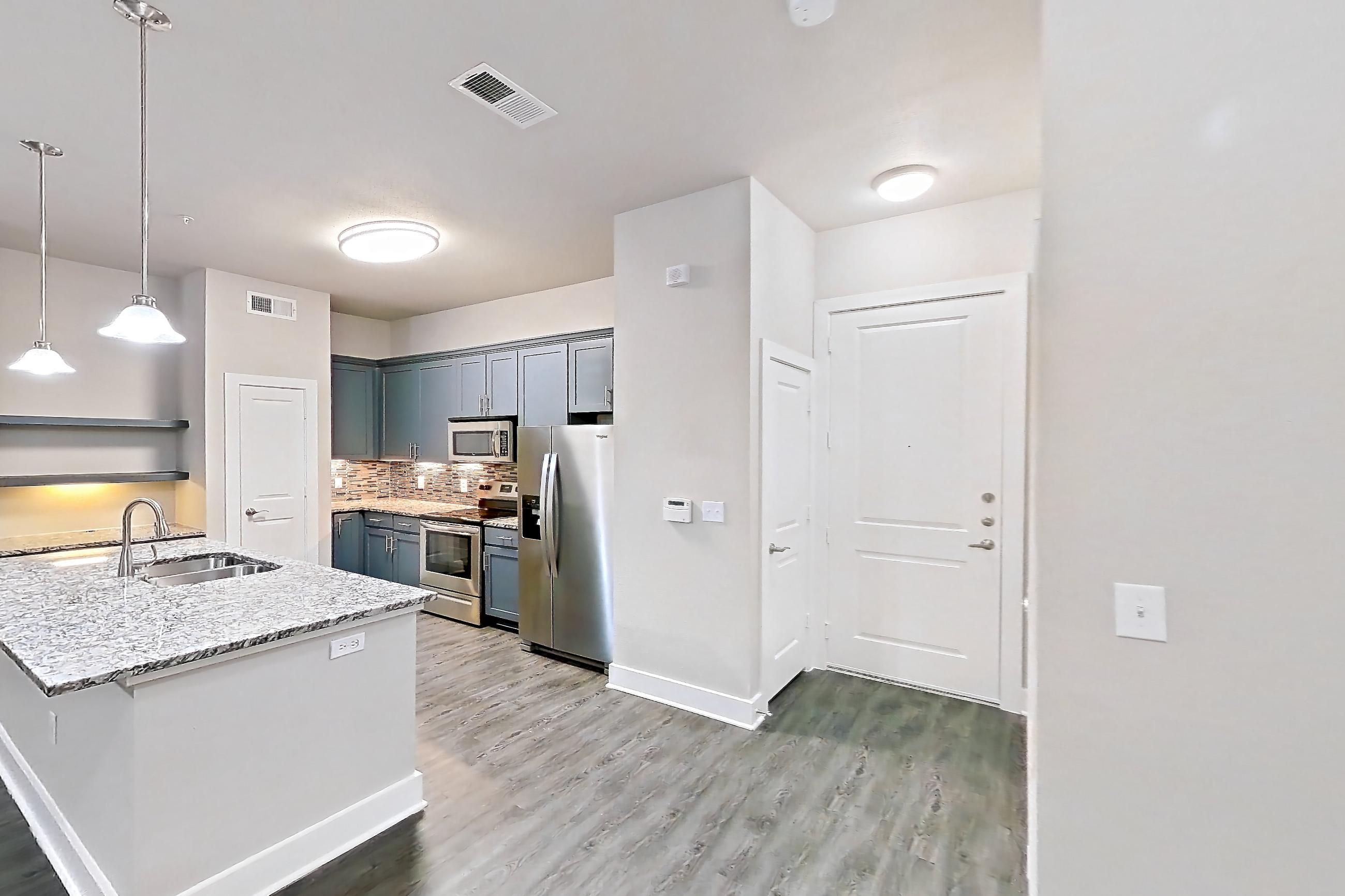 Dining room with dark wood-finish flooring, electric range, kitchen island, light stone countertops, oven/range, refrigerator, and stainless steel appliances, Apartment 144 at Voyager at the Space Center