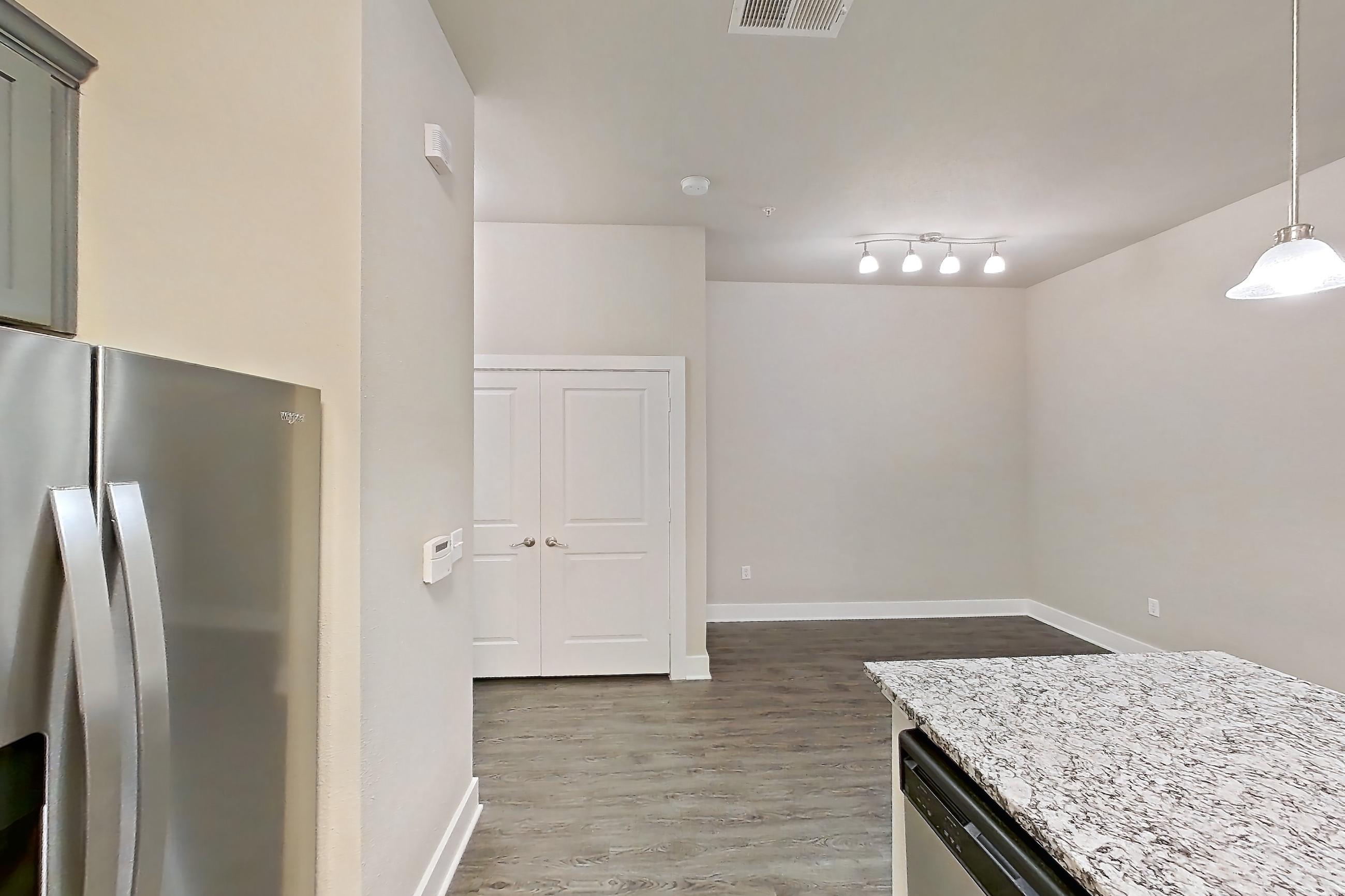 Kitchen with dark wood-finish flooring, dishwasher, electric range, kitchen island, light countertops, light stone countertops, light wood-finish flooring, microwave, oven/range, refrigerator, stainless steel appliances, and water & ice dispenser, Apartment 144 at Voyager at the Space Center