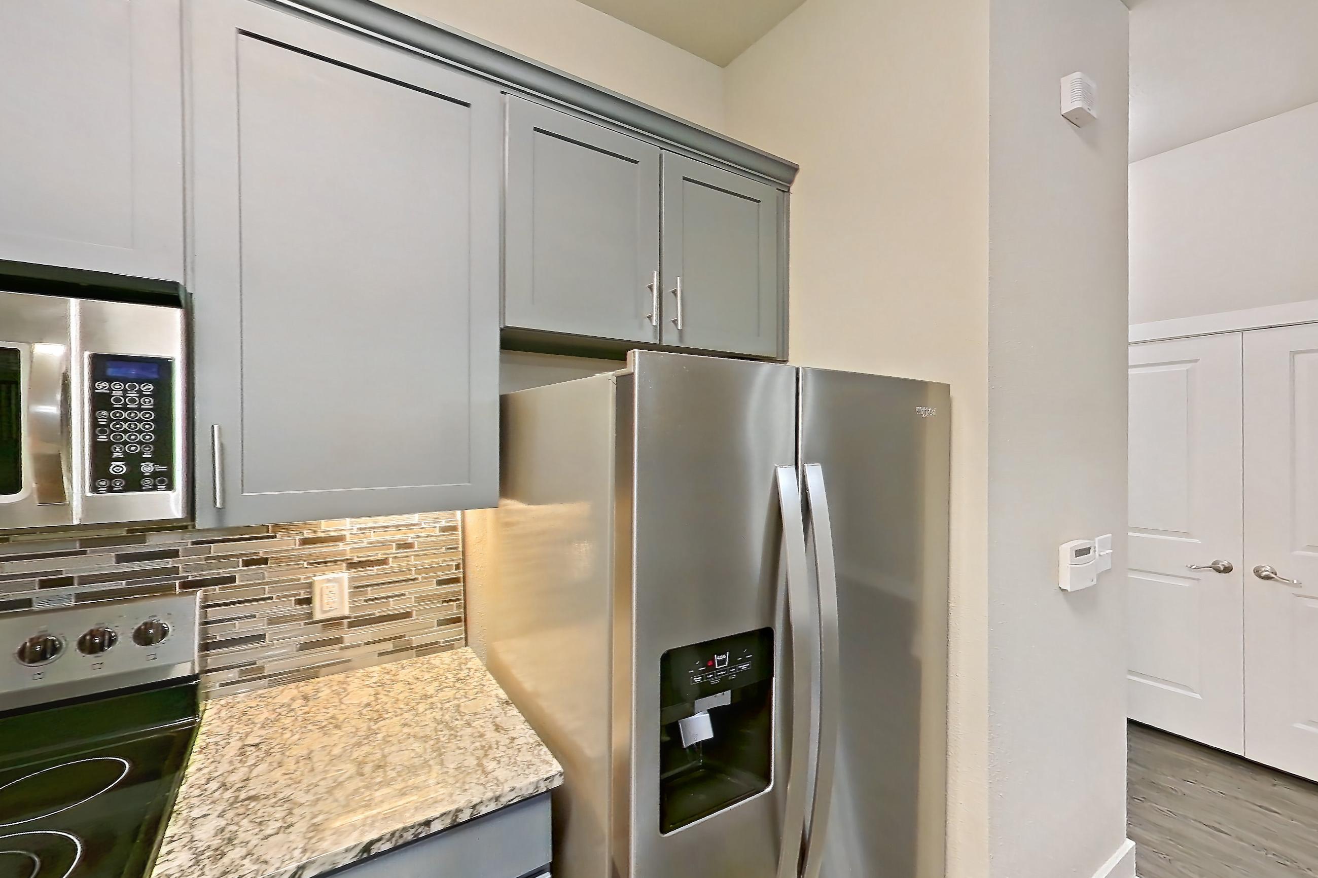 Kitchen with dark wood-finish flooring, dishwasher, electric range, kitchen island, light countertops, light stone countertops, light wood-finish flooring, microwave, oven/range, refrigerator, stainless steel appliances, and water & ice dispenser, Apartment 144 at Voyager at the Space Center