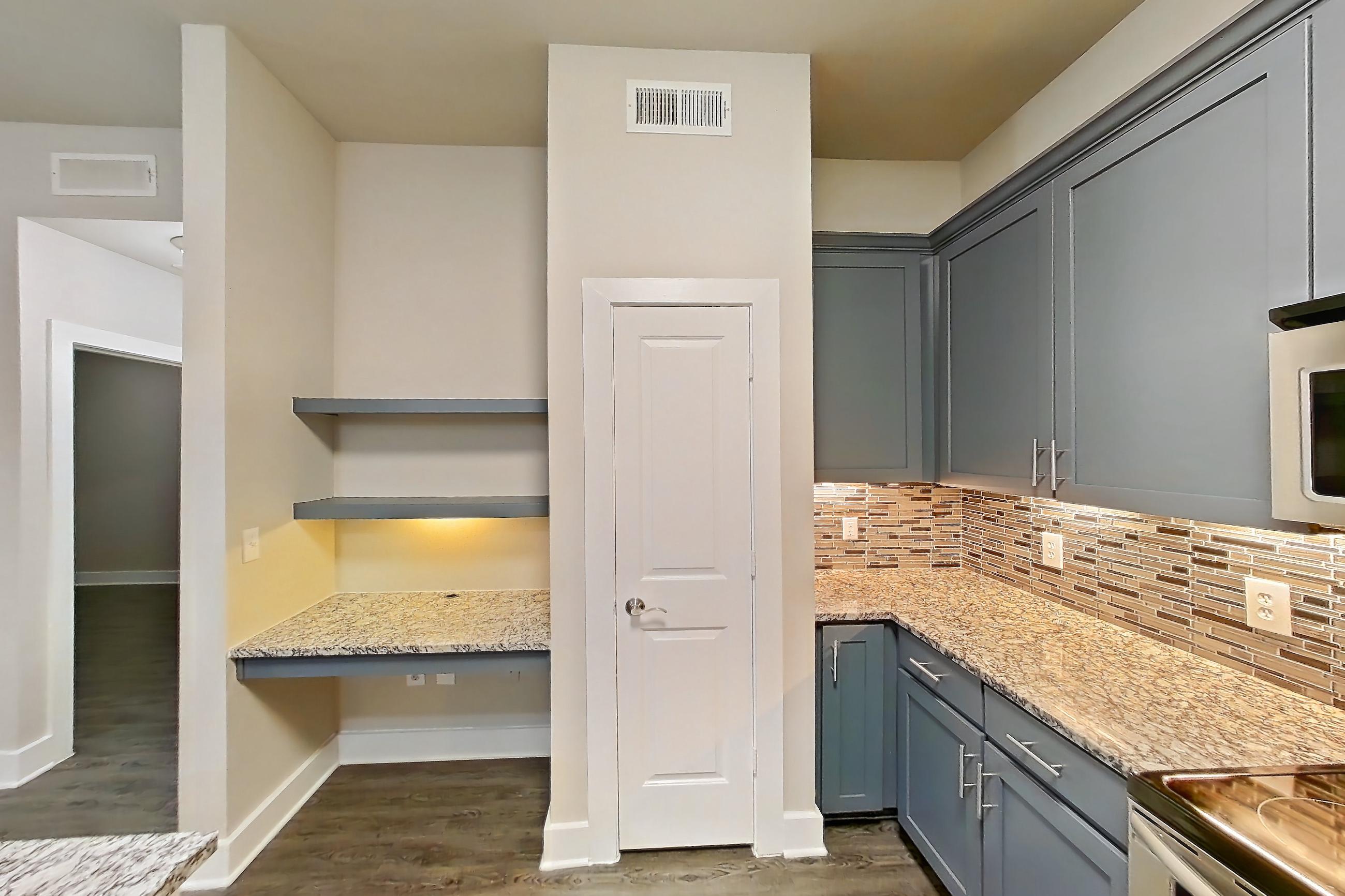 Kitchen with dark wood-finish flooring, dishwasher, electric range, kitchen island, light countertops, light stone countertops, light wood-finish flooring, microwave, oven/range, refrigerator, stainless steel appliances, and water & ice dispenser, Apartment 144 at Voyager at the Space Center