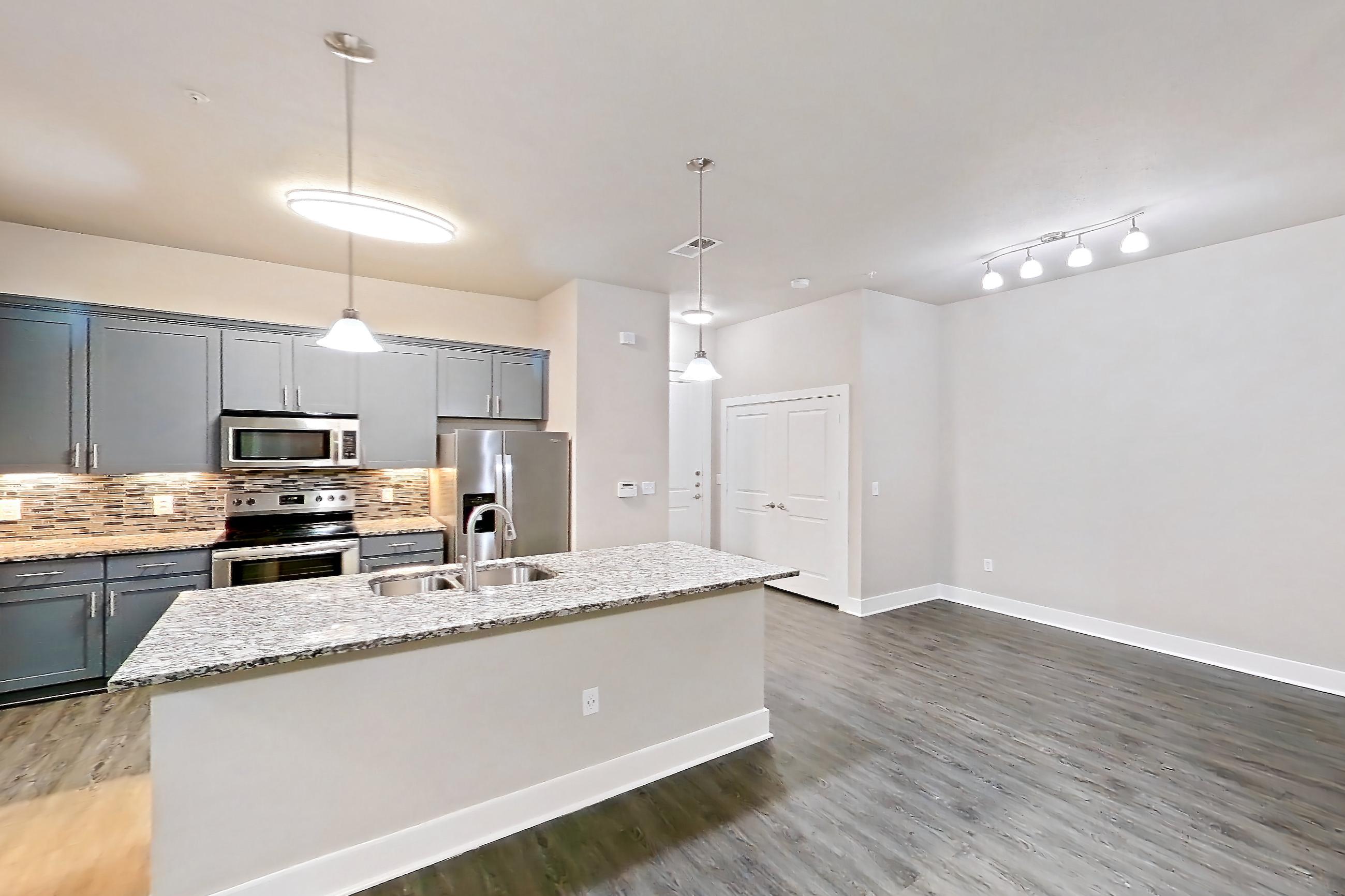 Living space with dark wood-finish flooring, electric range, kitchen island, light stone countertops, oven/range, refrigerator, stainless steel appliances, and water & ice dispenser, Apartment 144 at Voyager at the Space Center