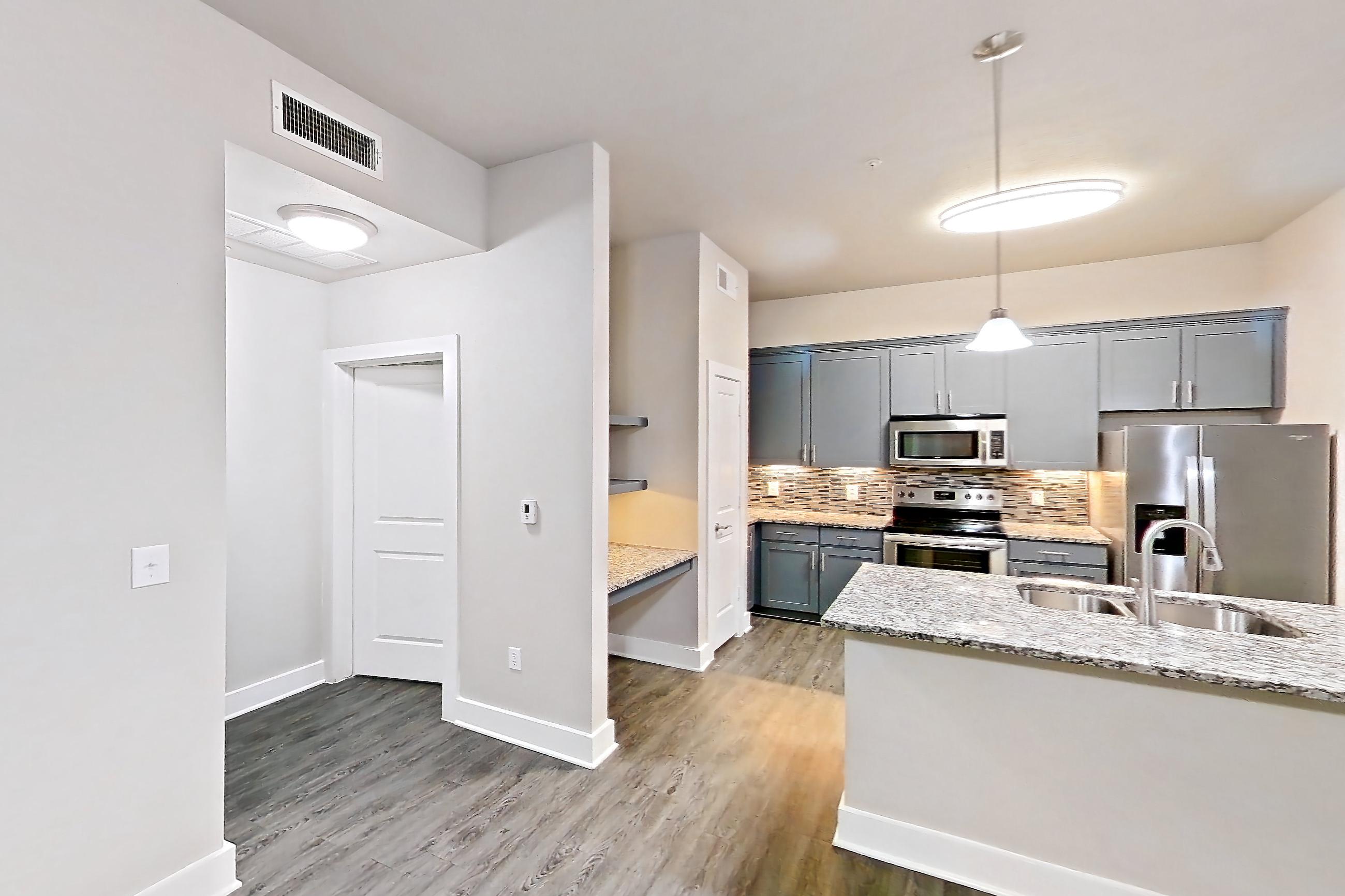 Living space with dark wood-finish flooring, electric range, kitchen island, light stone countertops, oven/range, refrigerator, stainless steel appliances, and water & ice dispenser, Apartment 144 at Voyager at the Space Center