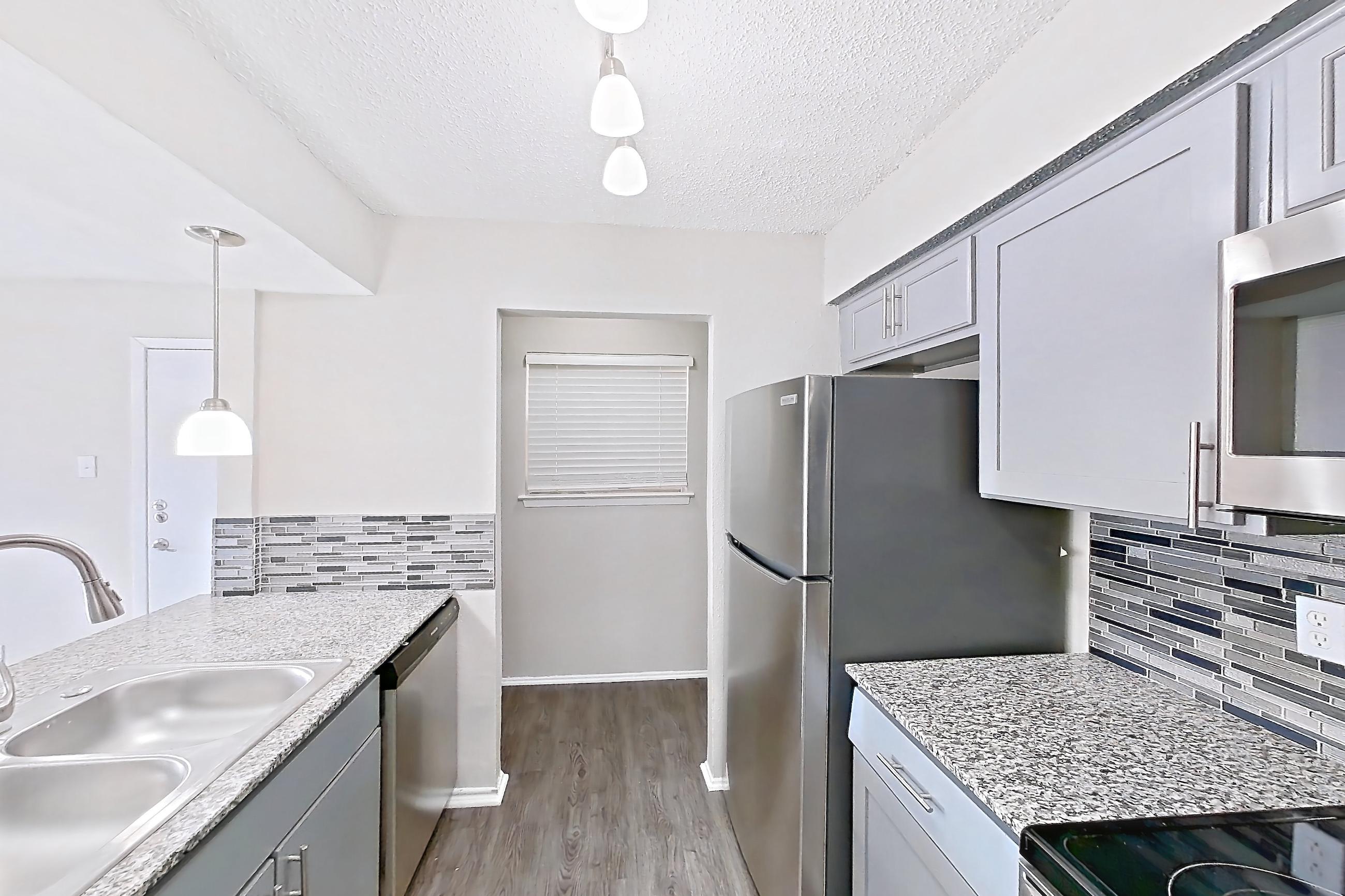 Kitchen with dark wood-finish flooring, dishwasher, electric range, light countertops, light stone countertops, microwave, oven/range, refrigerator, and stainless steel appliances, Apartment 236ND at The Cassidy at Western Hills