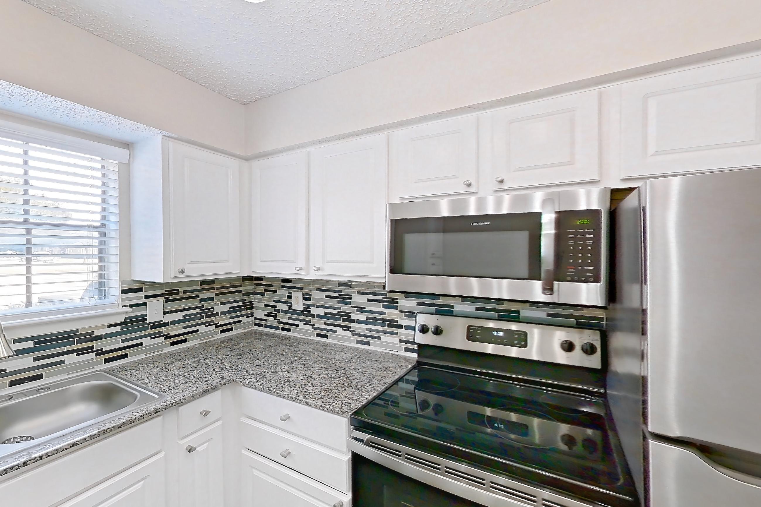 Kitchen with dark wood-finish flooring, dishwasher, electric range, light countertops, light stone countertops, microwave, oven/range, refrigerator, and stainless steel appliances, Apartment 1011 at Creekside Village
