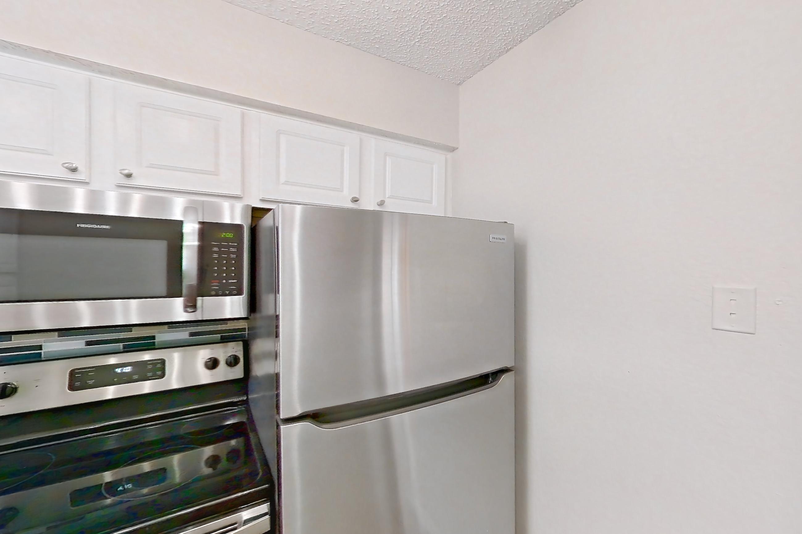 Kitchen with dark wood-finish flooring, dishwasher, electric range, light countertops, light stone countertops, microwave, oven/range, refrigerator, and stainless steel appliances, Apartment 1011 at Creekside Village