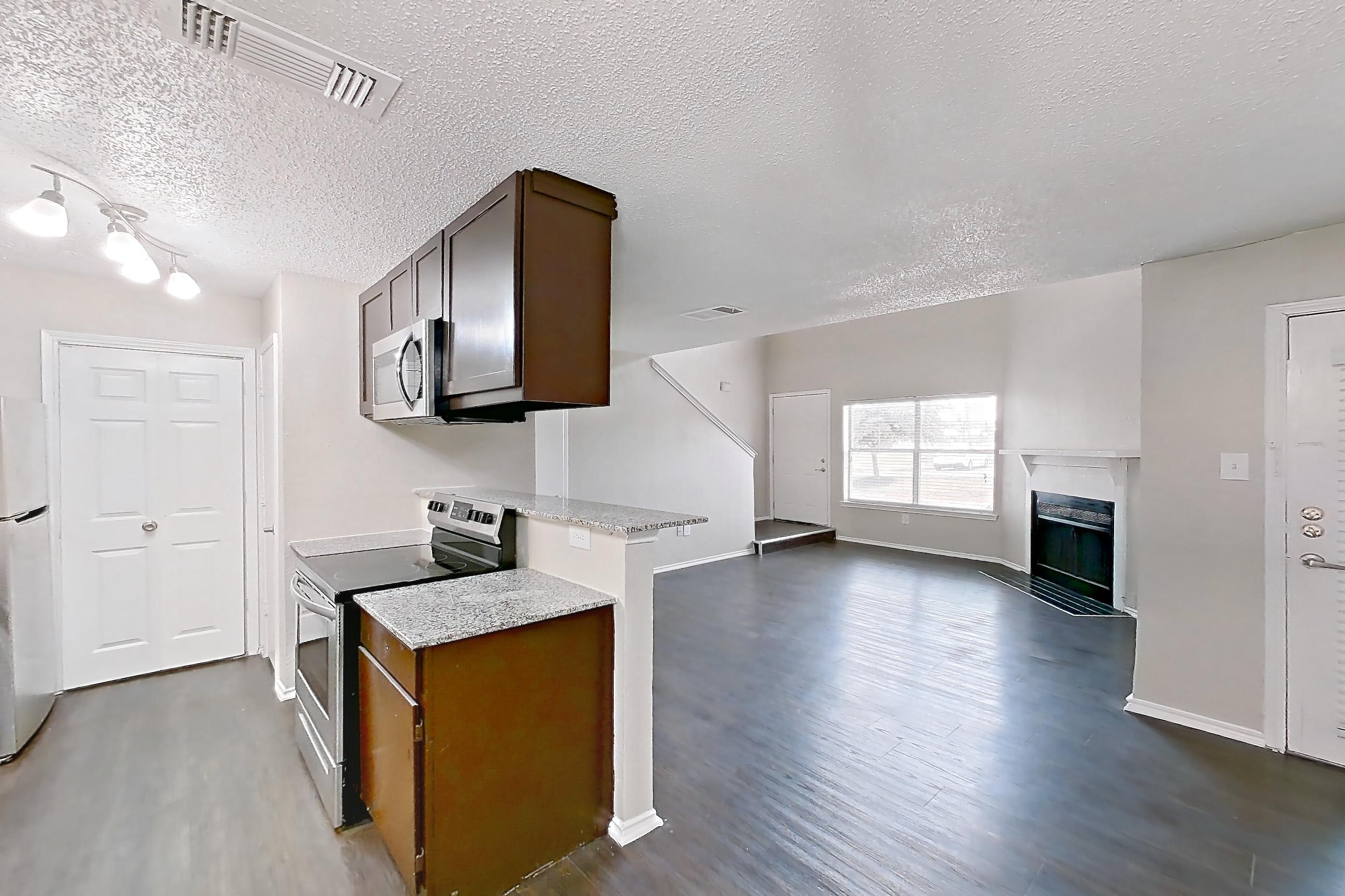Dining room with dark wood-finish flooring, electric range, fireplace, light stone countertops, oven/range, and stainless steel appliances, Apartment 103 at Quail Ridge Apartments