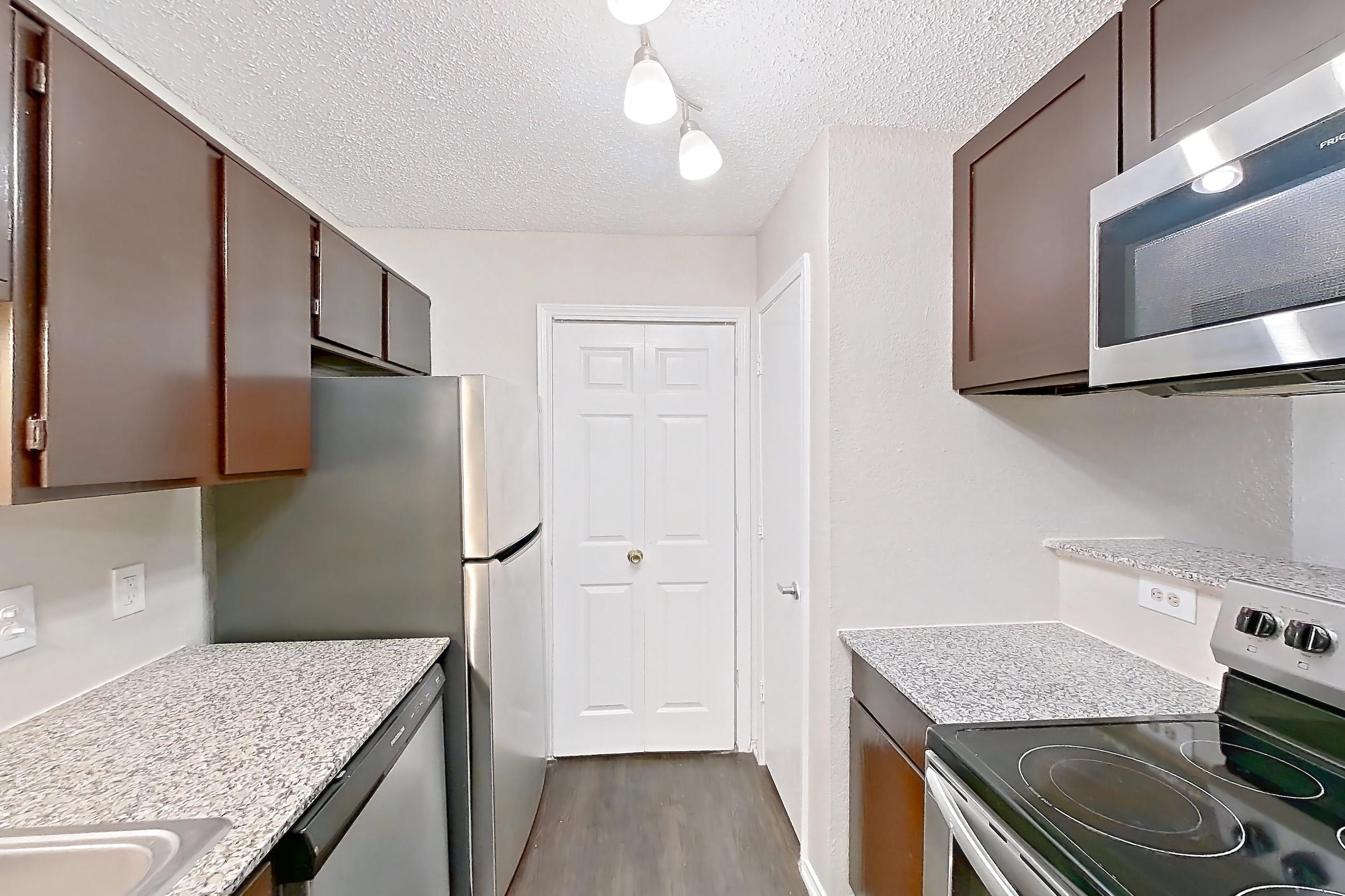 Kitchen with dark wood-finish flooring, dishwasher, electric range, light countertops, light stone countertops, microwave, oven/range, refrigerator, and stainless steel appliances, Apartment 103 at Quail Ridge Apartments