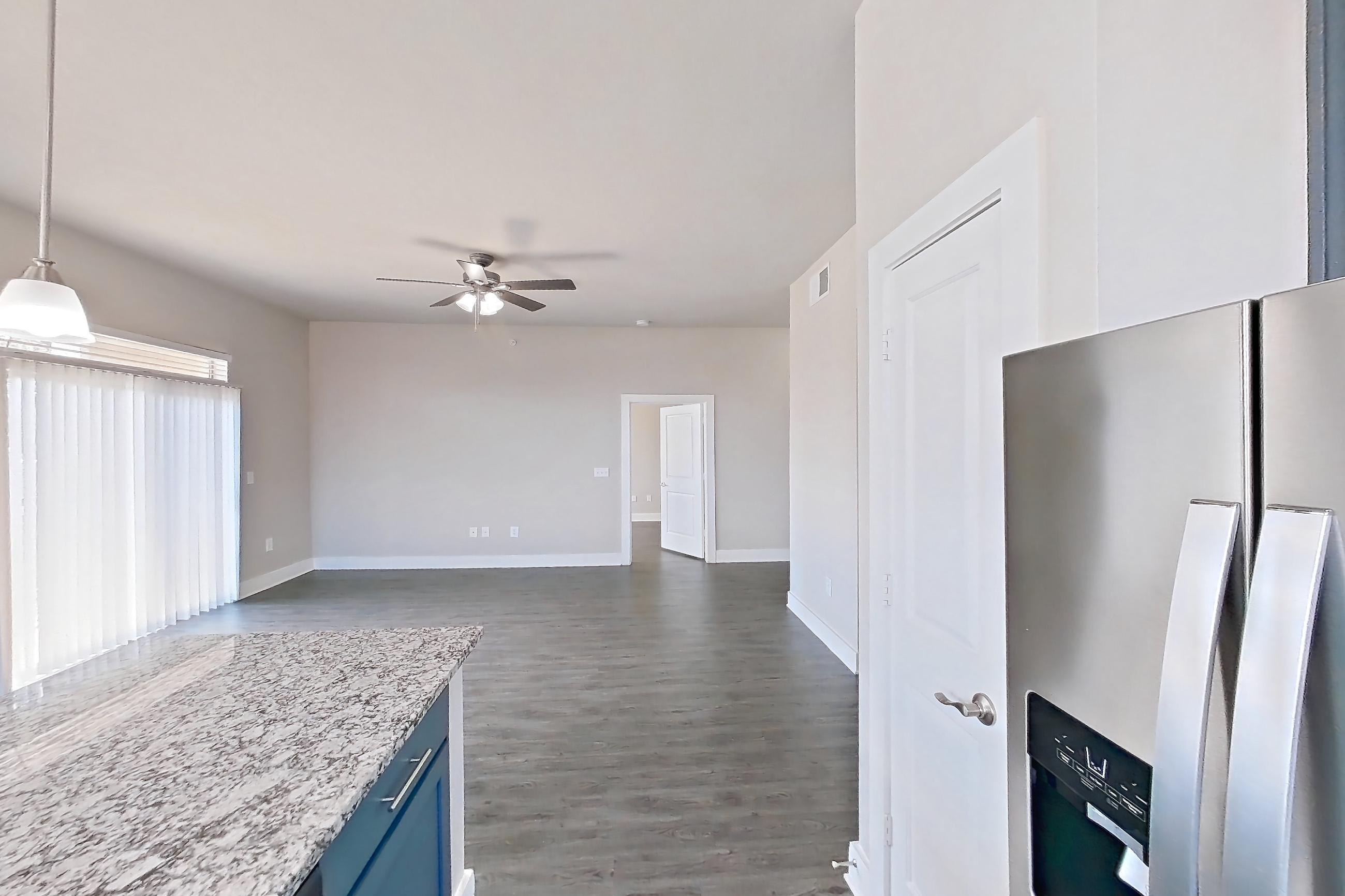 Kitchen with dark wood-finish flooring, dishwasher, electric range, kitchen island, light countertops, light stone countertops, oven/range, refrigerator, stainless steel appliances, and water & ice dispenser, Apartment 356 at Voyager at the Space Center