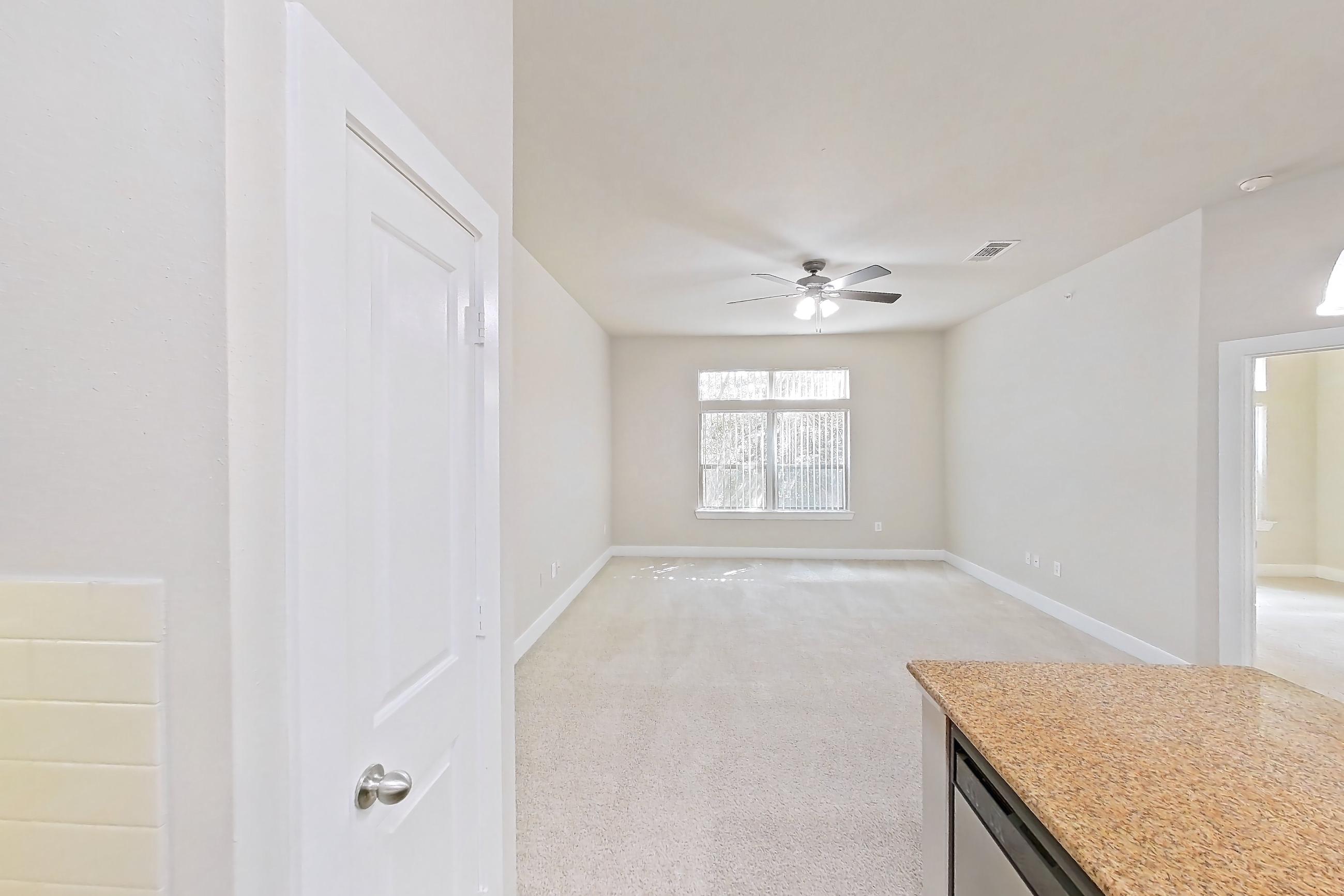 Kitchen with black appliances, dishwasher, electric range, kitchen island, light carpet, light stone countertops, light wood-finish flooring, microwave, oven/range, and stainless steel appliances, Apartment 373 at Voyager at the Space Center