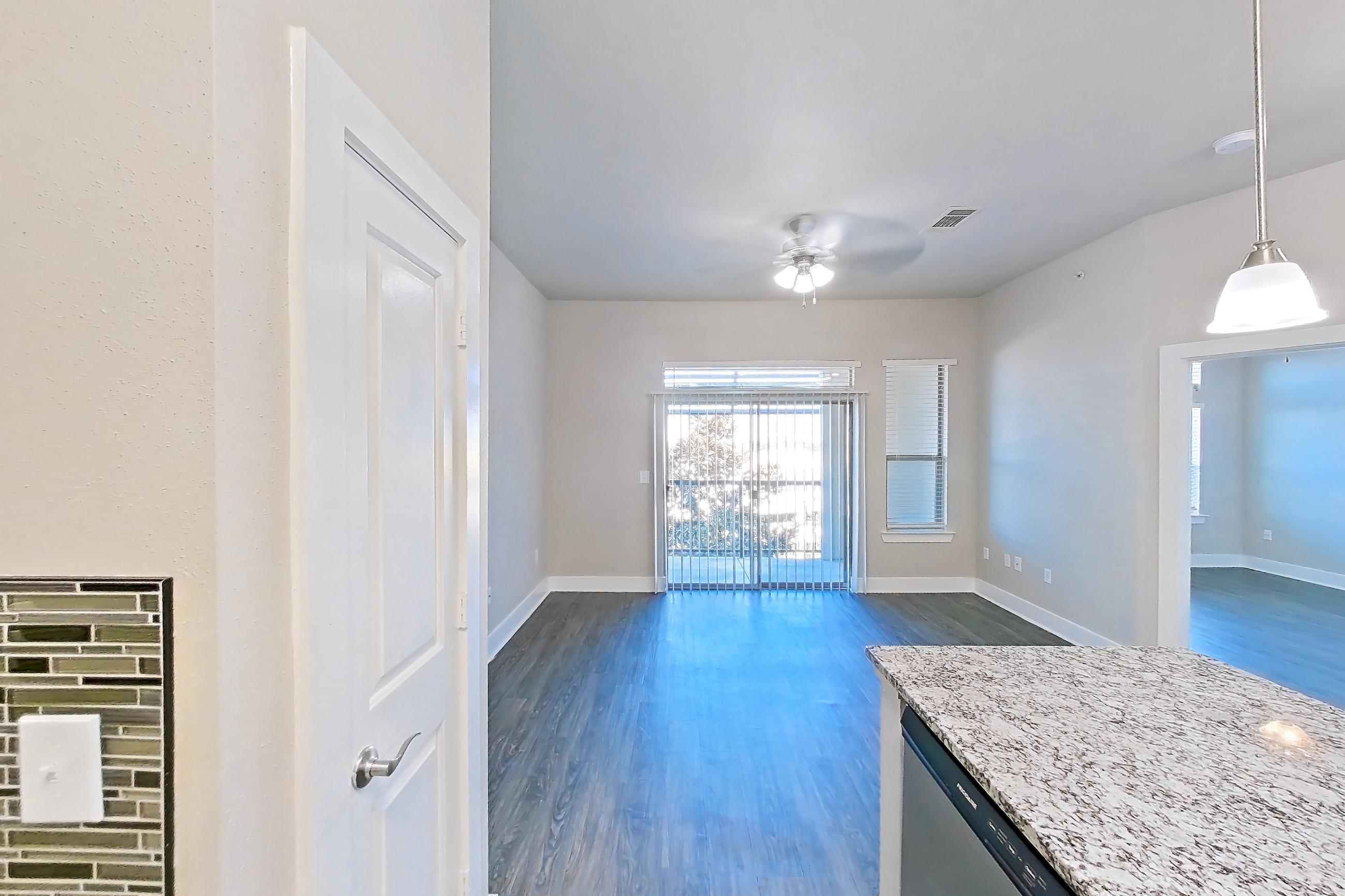 Kitchen with dark wood-finish flooring, dishwasher, electric range, kitchen island, light countertops, light stone countertops, light wood-finish flooring, microwave, oven/range, and stainless steel appliances, Apartment 410 at Voyager at the Space Center