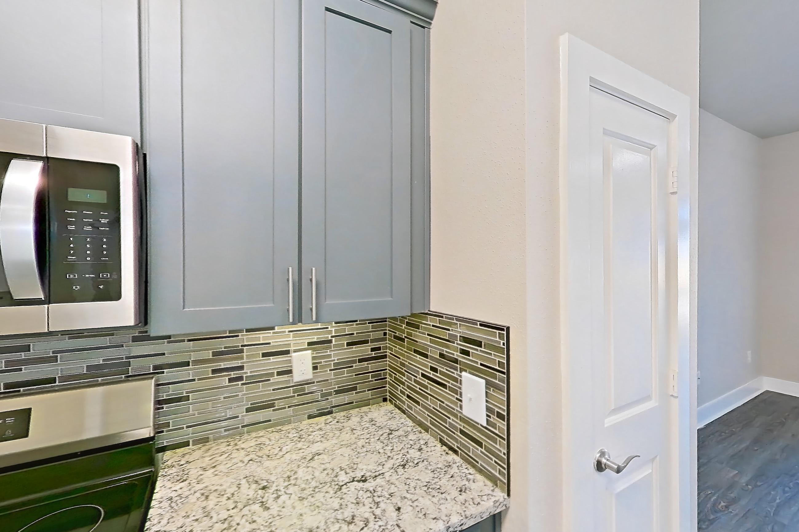 Kitchen with dark wood-finish flooring, dishwasher, electric range, kitchen island, light countertops, light stone countertops, light wood-finish flooring, microwave, oven/range, and stainless steel appliances, Apartment 410 at Voyager at the Space Center