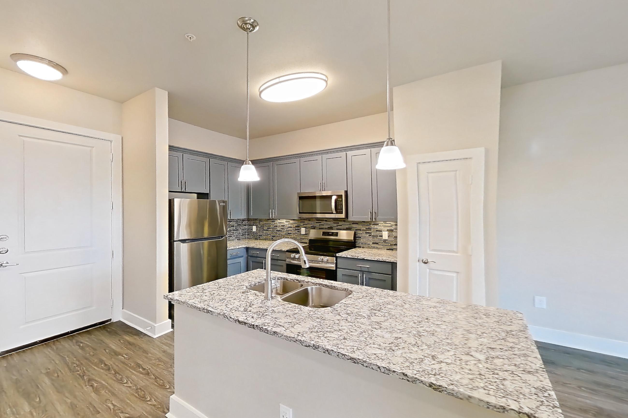 Living space with dark wood-finish flooring, electric range, kitchen island, light stone countertops, oven/range, and stainless steel appliances, Apartment 410 at Voyager at the Space Center