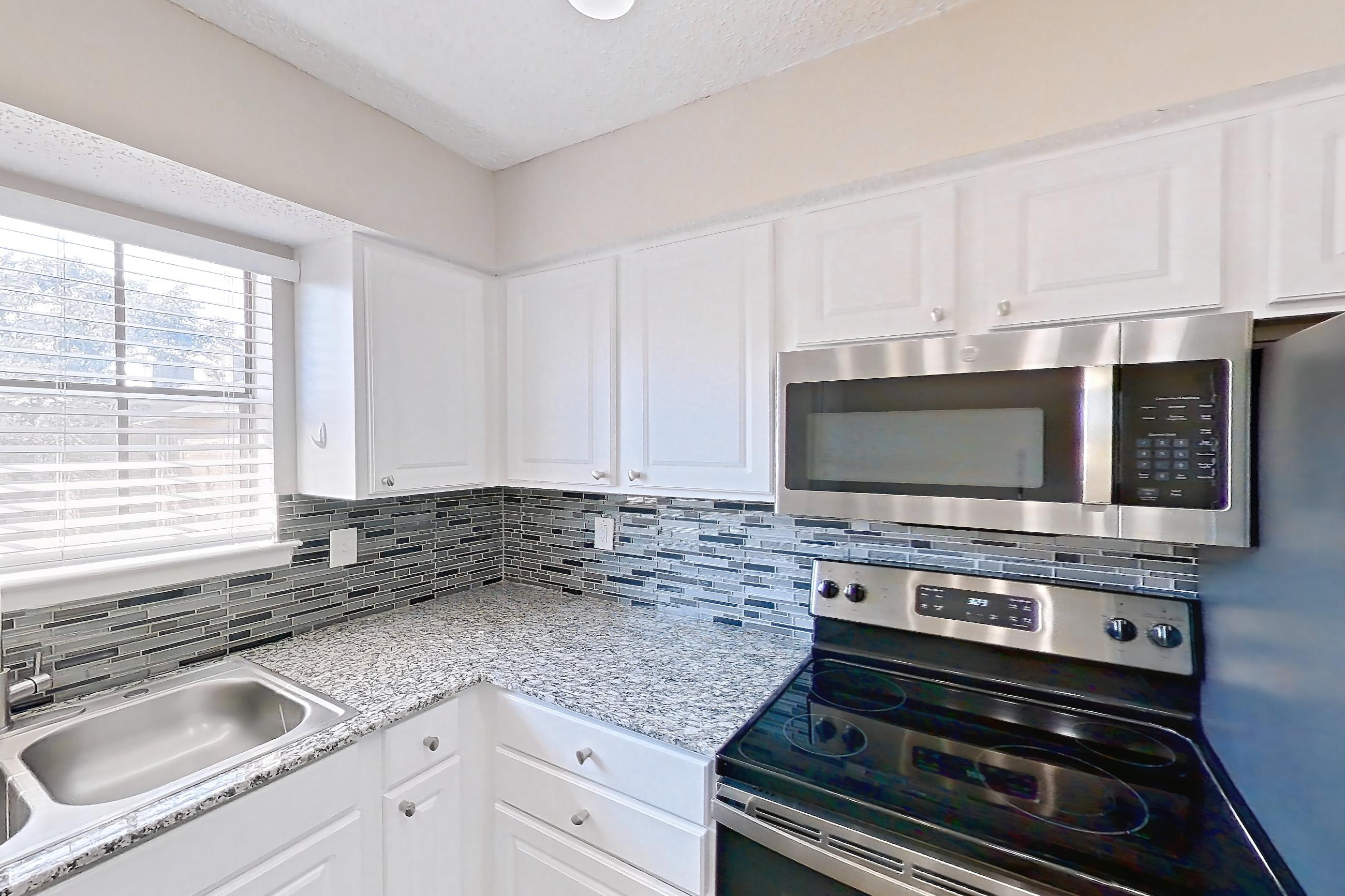 Kitchen with dark wood-finish flooring, dishwasher, electric range, light countertops, light stone countertops, microwave, oven/range, refrigerator, and stainless steel appliances, Apartment 2181 at Creekside Village