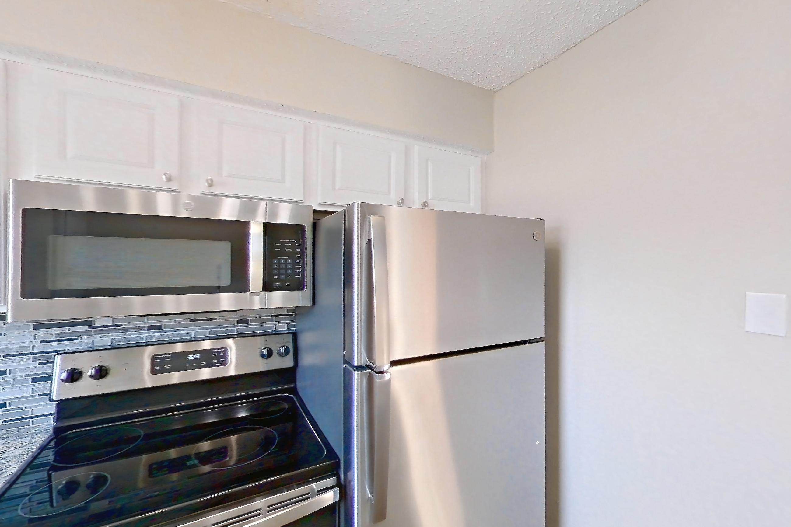 Kitchen with dark wood-finish flooring, dishwasher, electric range, light countertops, light stone countertops, microwave, oven/range, refrigerator, and stainless steel appliances, Apartment 2181 at Creekside Village