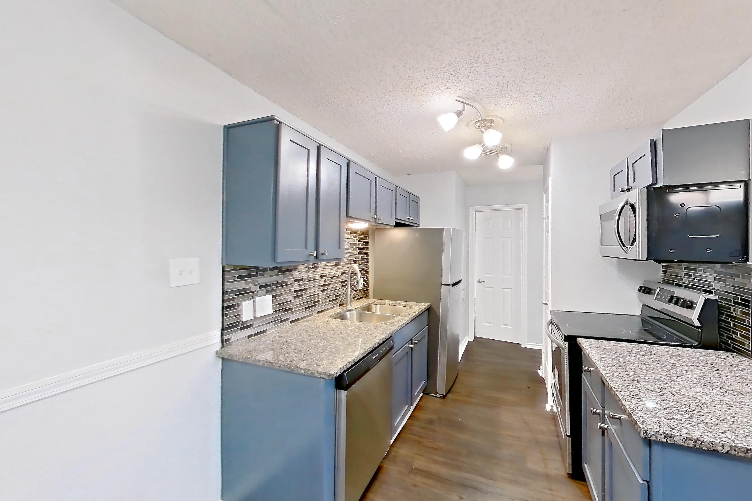 Dining room with dark wood-finish flooring, dishwasher, electric range, fireplace, light countertops, light stone countertops, oven/range, refrigerator, and stainless steel appliances, Apartment 506 at Quail Ridge Apartments