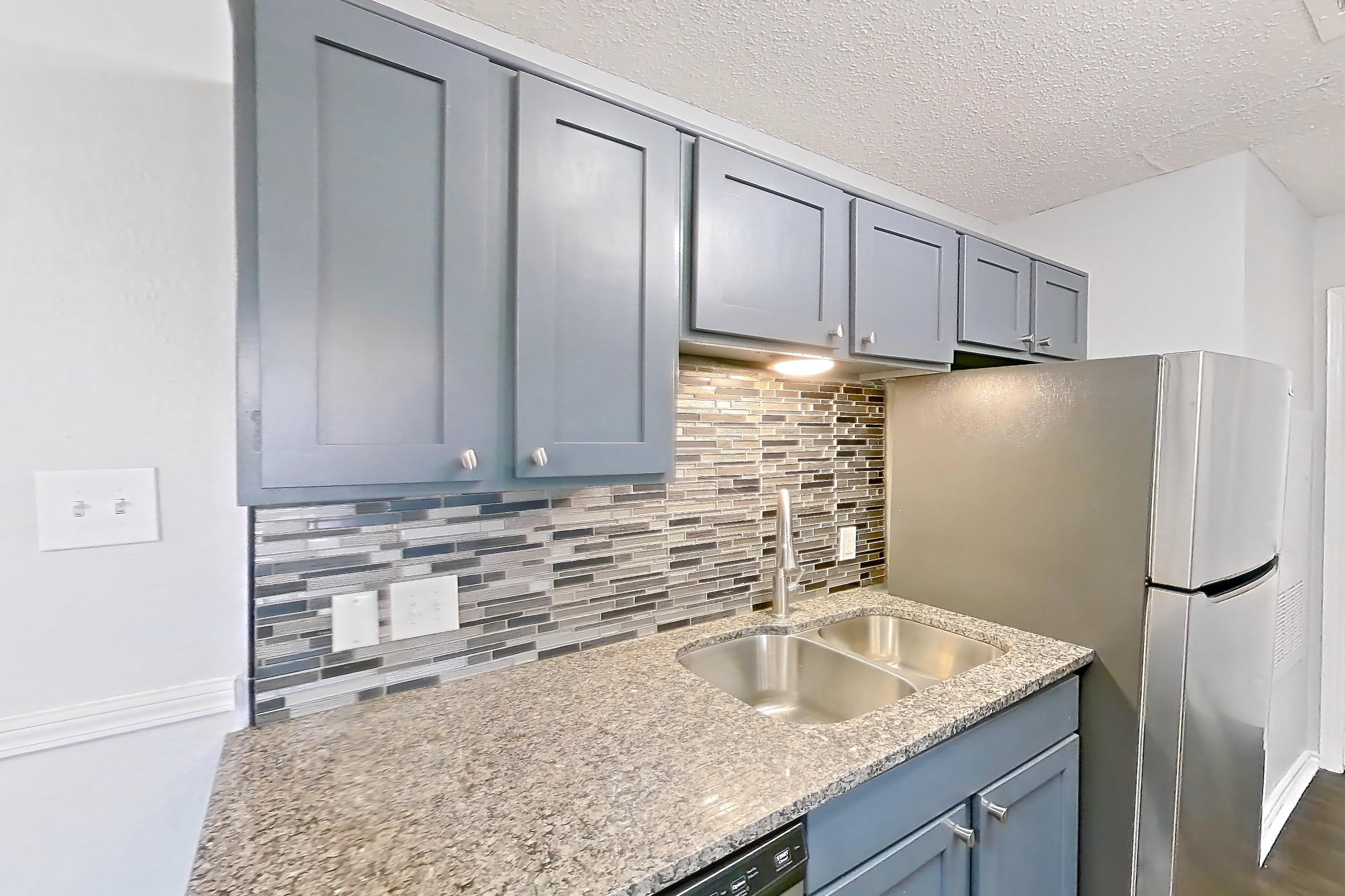 Kitchen with dark wood-finish flooring, dishwasher, electric range, fireplace, light countertops, light stone countertops, oven/range, refrigerator, and stainless steel appliances, Apartment 506 at Quail Ridge Apartments