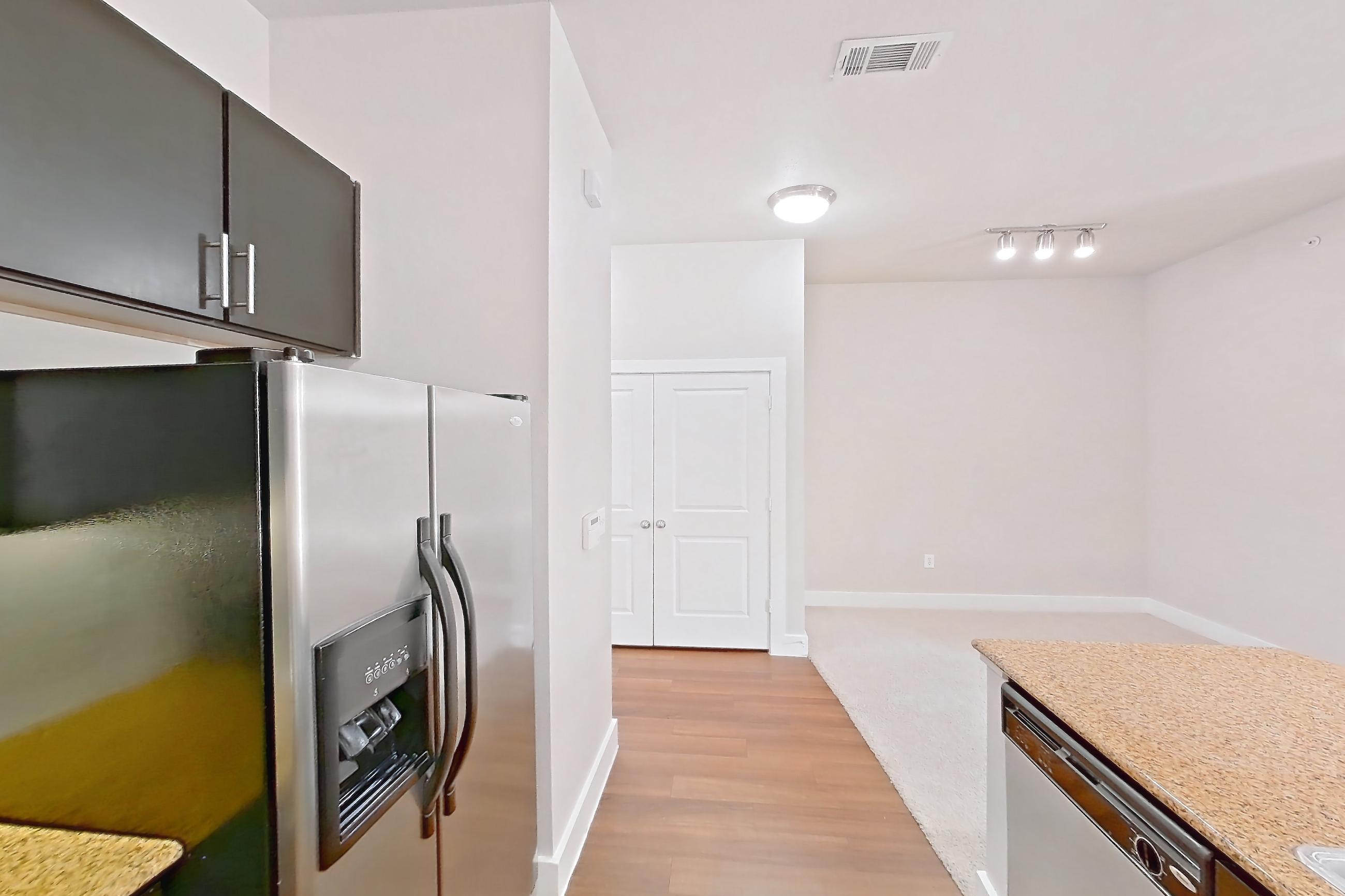 Kitchen with dishwasher, electric range, kitchen island, light countertops, light stone countertops, light wood-finish flooring, microwave, oven/range, refrigerator, stainless steel appliances, and water & ice dispenser, Apartment 444 at Voyager at the Space Center