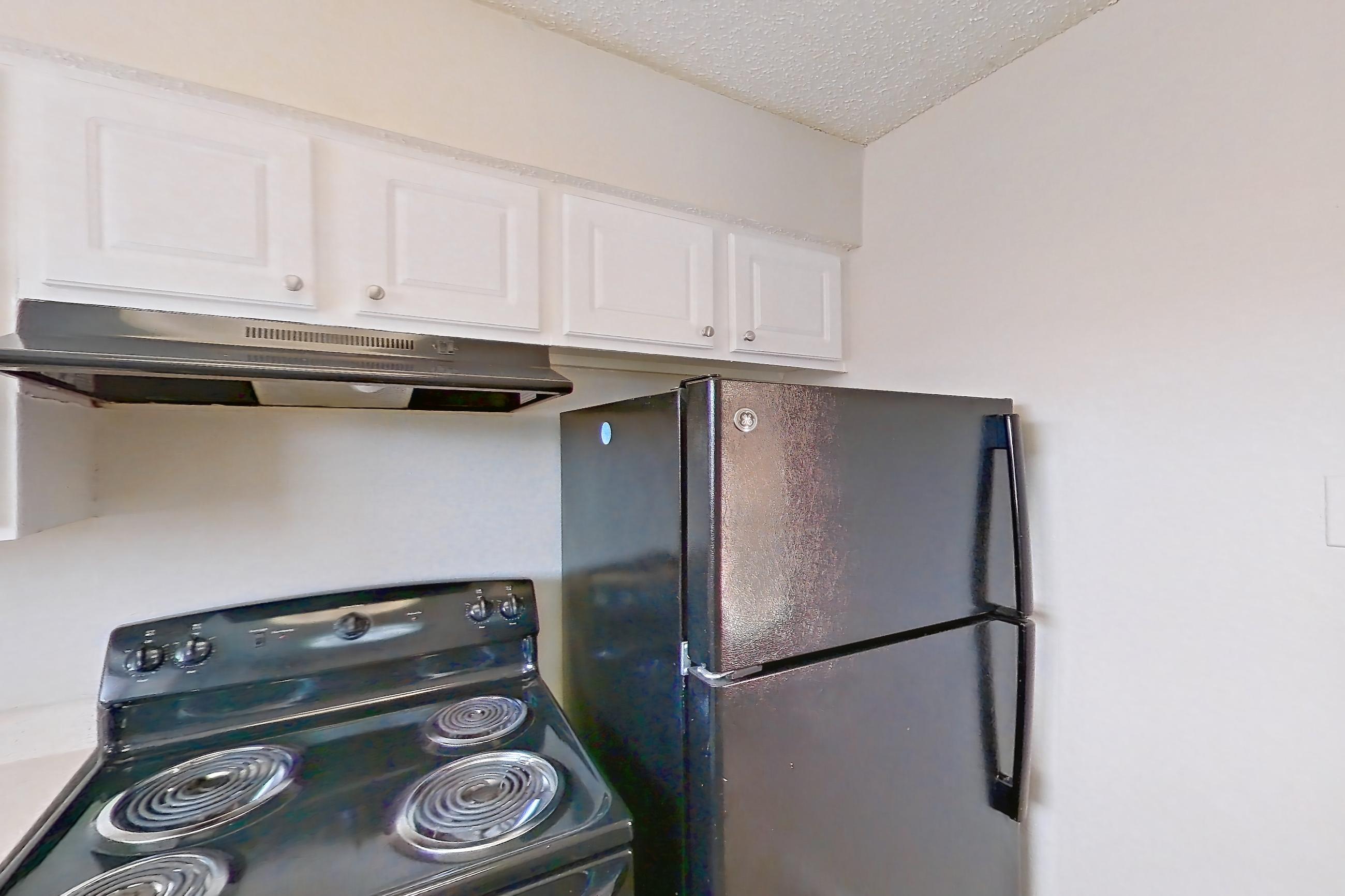 Kitchen with black appliances, dishwasher, electric range, light countertops, light wood-finish flooring, oven/range, range hood, and refrigerator, Apartment 2219 at Creekside Village