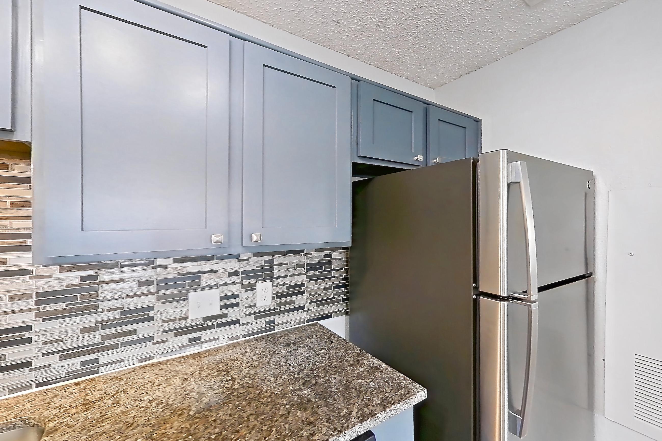 Kitchen with dark stone countertops, dark wood-finish flooring, dishwasher, electric range, light countertops, light wood-finish flooring, oven/range, refrigerator, and stainless steel appliances, Apartment 509 at Quail Ridge Apartments