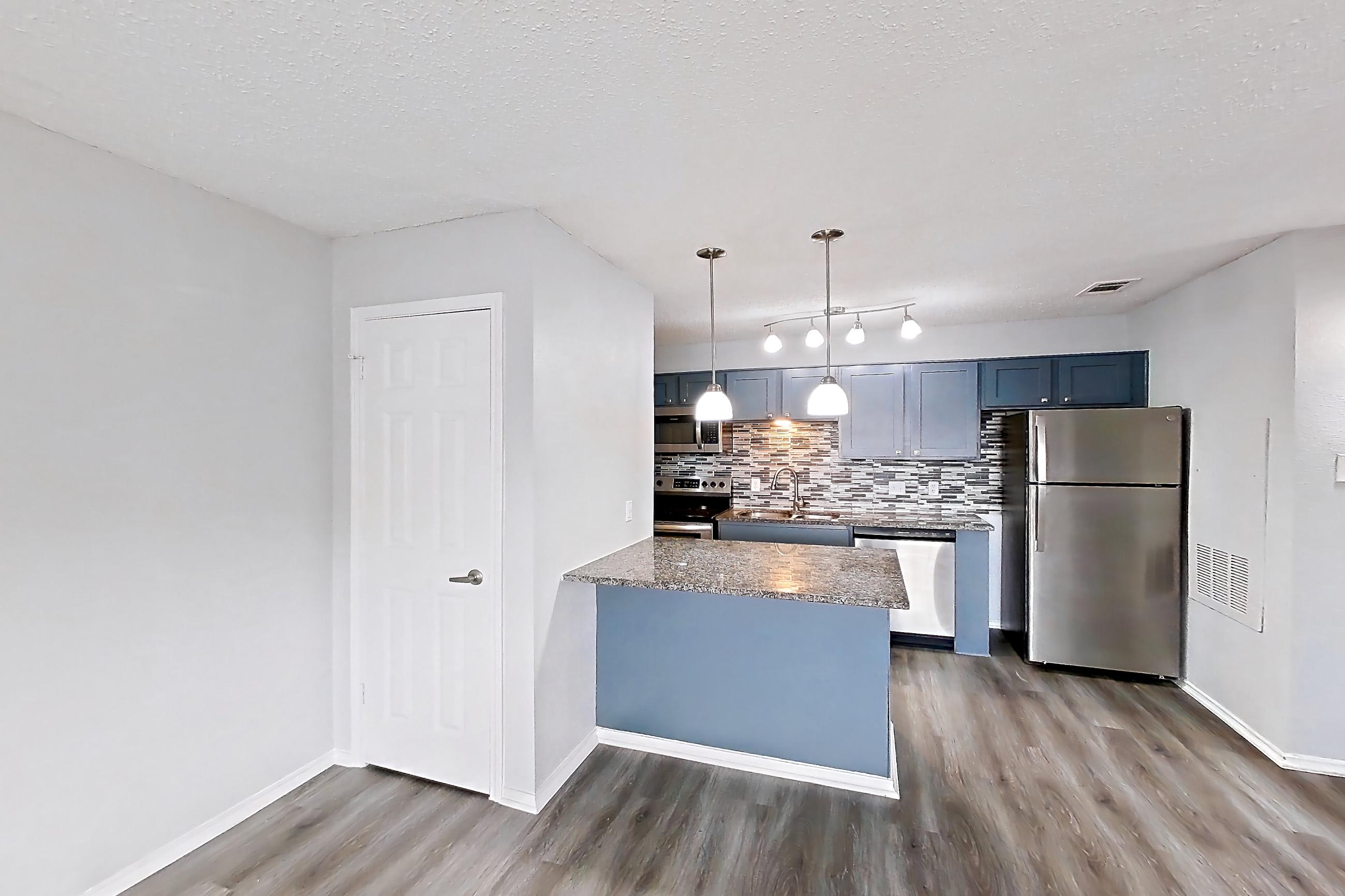 Living room with dark stone countertops, dark wood-finish flooring, dishwasher, electric range, light countertops, light wood-finish flooring, oven/range, refrigerator, and stainless steel appliances, Apartment 509 at Quail Ridge Apartments