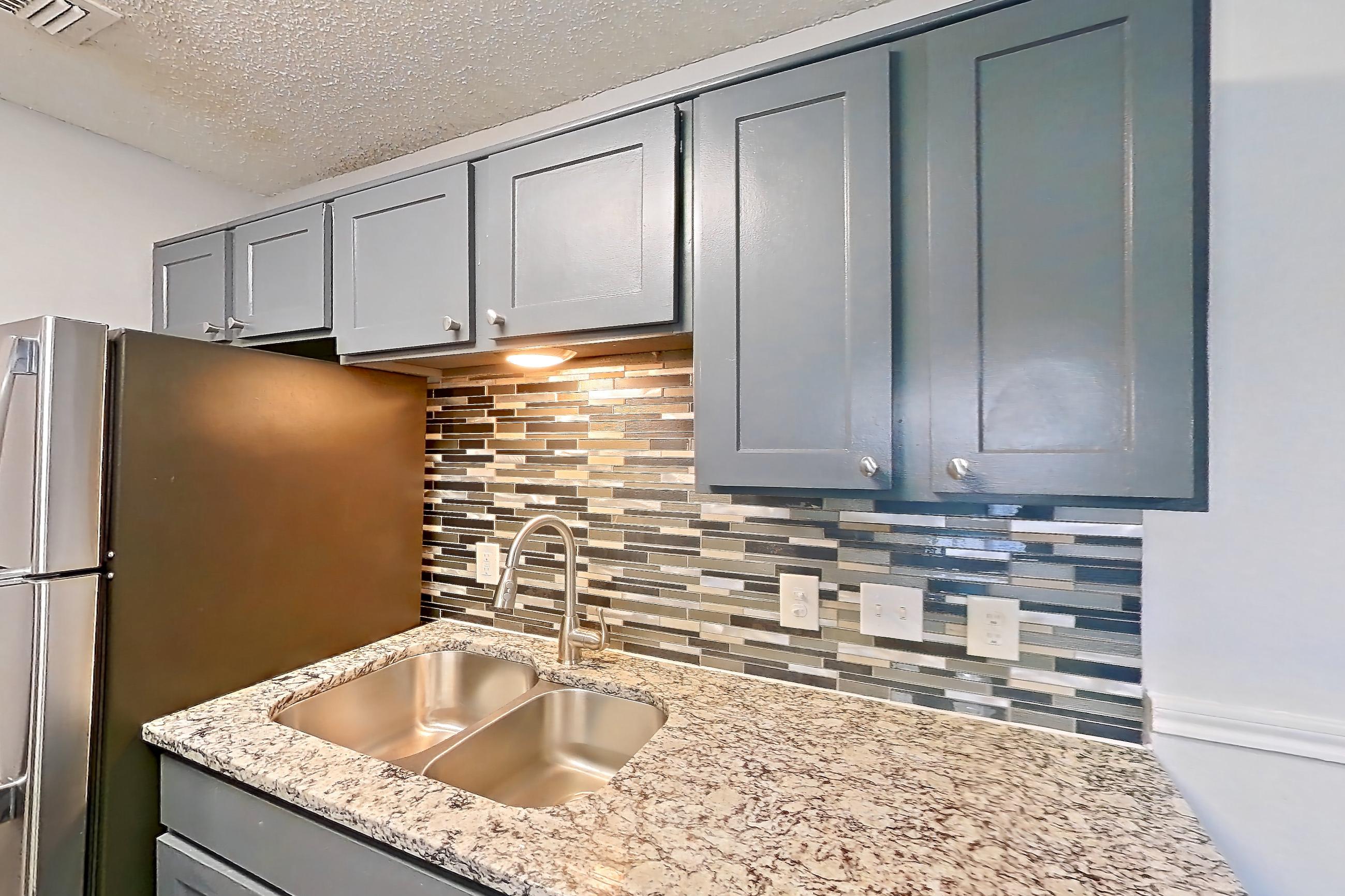 Kitchen with dark wood-finish flooring, dishwasher, electric range, fireplace, light countertops, light stone countertops, light wood-finish flooring, oven/range, refrigerator, and stainless steel appliances, Apartment 811 at Quail Ridge Apartments