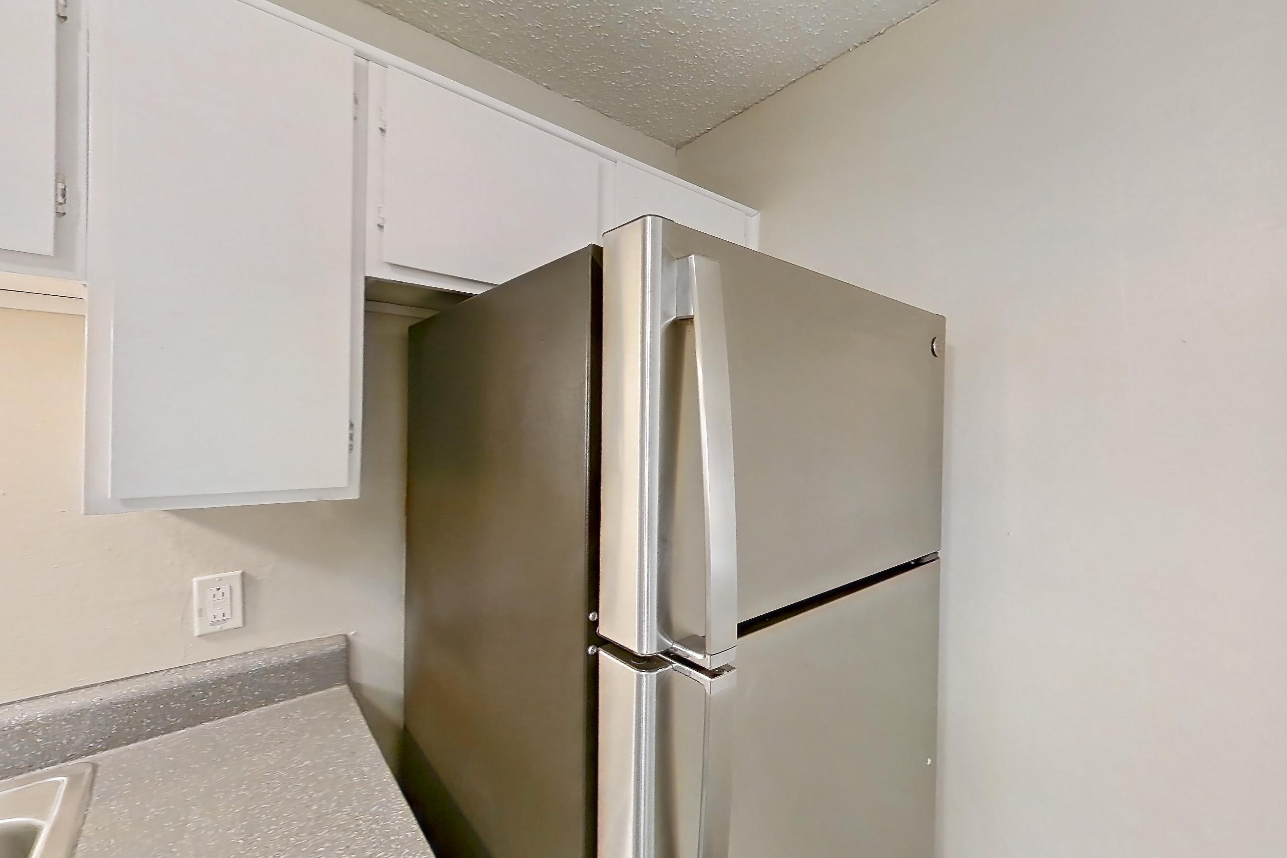 Kitchen with black appliances, dark countertops, dark wood-finish flooring, dishwasher, electric range, light countertops, light wood-finish flooring, oven/range, range hood, refrigerator, and stainless steel appliances, Apartment 1904 at Quail Ridge Apartments