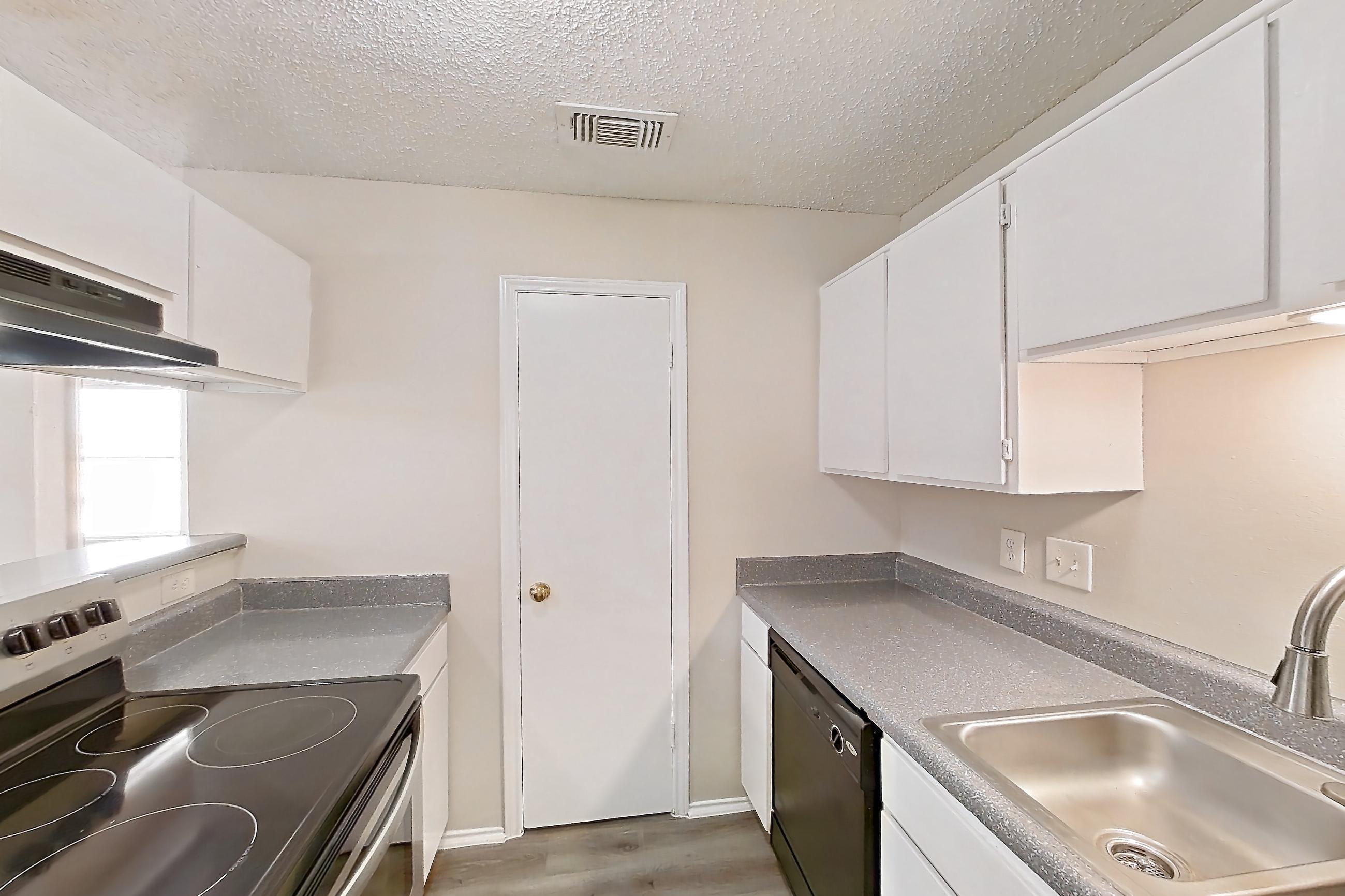 Kitchen with black appliances, dark countertops, dark wood-finish flooring, dishwasher, electric range, light countertops, light wood-finish flooring, oven/range, range hood, refrigerator, and stainless steel appliances, Apartment 1904 at Quail Ridge Apartments