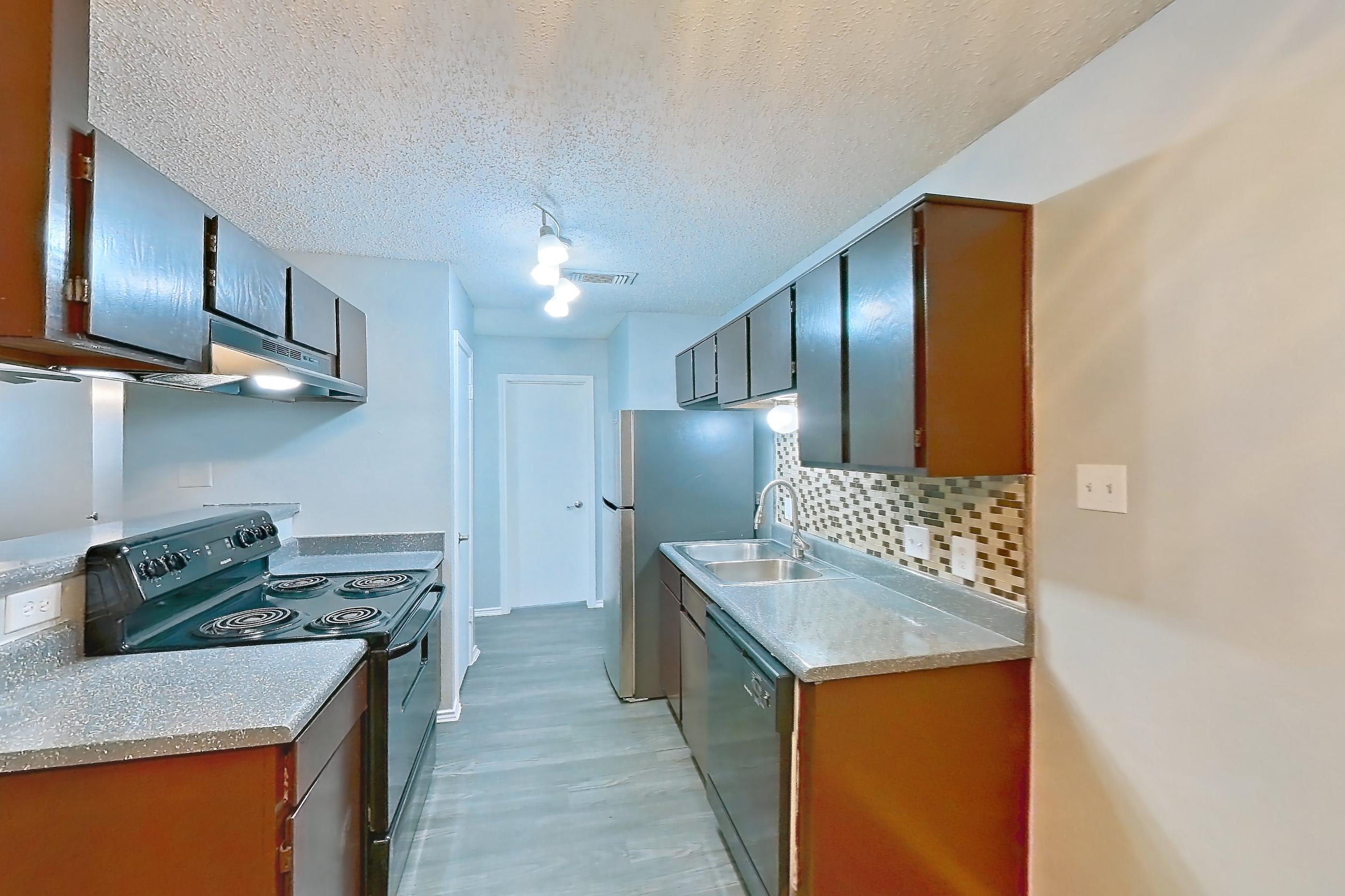 Dining room with black appliances, dark wood-finish flooring, dishwasher, electric range, fireplace, light countertops, light wood-finish flooring, oven/range, and range hood, Apartment 2105 at Quail Ridge Apartments
