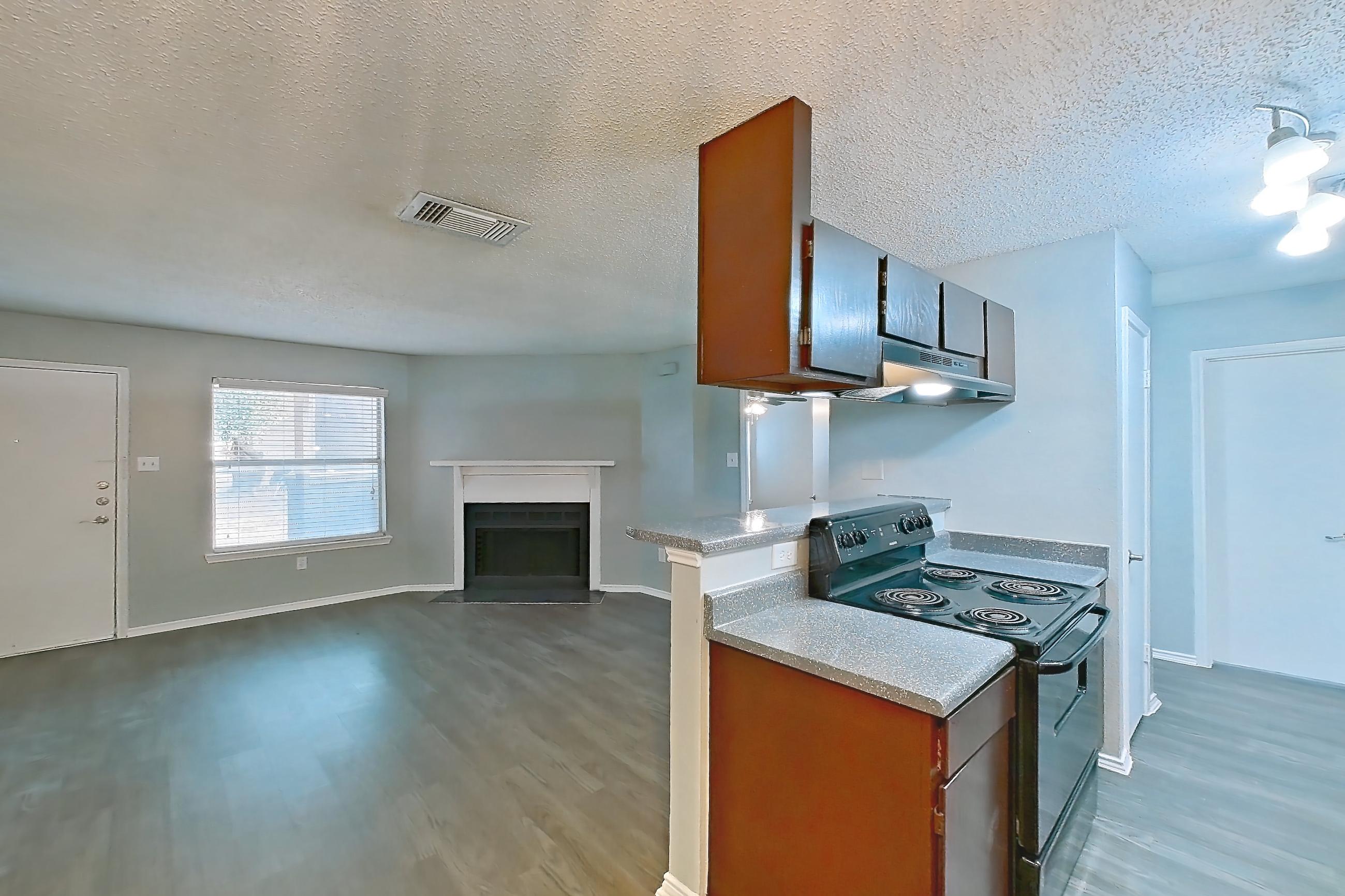 Dining room with black appliances, dark wood-finish flooring, dishwasher, electric range, fireplace, light countertops, light wood-finish flooring, oven/range, and range hood, Apartment 2105 at Quail Ridge Apartments