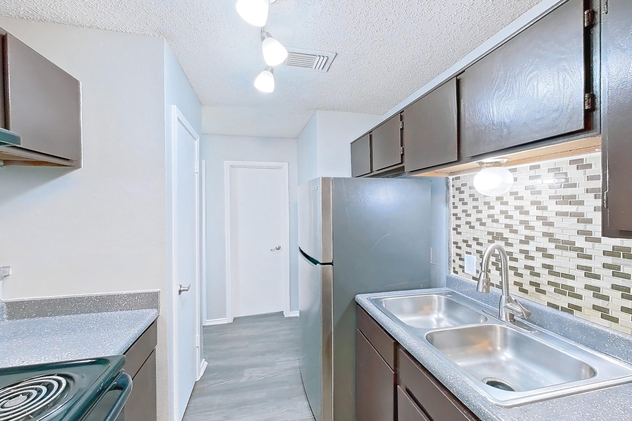 Kitchen with black appliances, dark countertops, dishwasher, electric range, light countertops, light wood-finish flooring, oven/range, range hood, refrigerator, and stainless steel appliances, Apartment 2105 at Quail Ridge Apartments