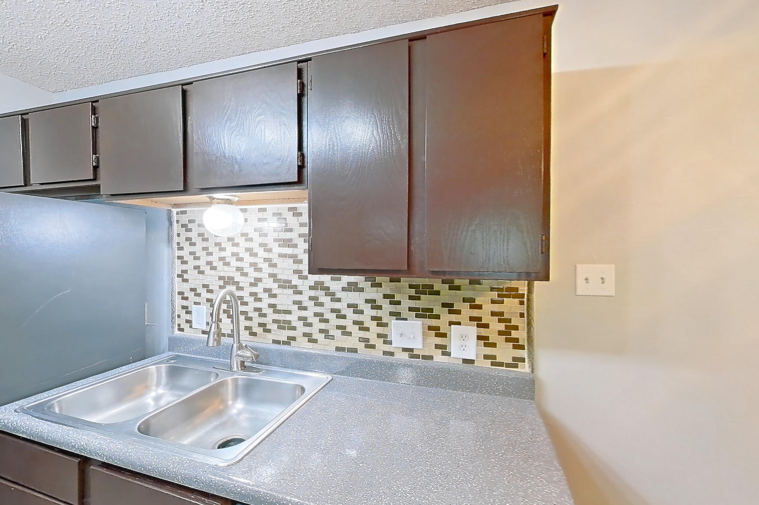 Kitchen with black appliances, dark countertops, dishwasher, electric range, light countertops, light wood-finish flooring, oven/range, range hood, refrigerator, and stainless steel appliances, Apartment 2105 at Quail Ridge Apartments